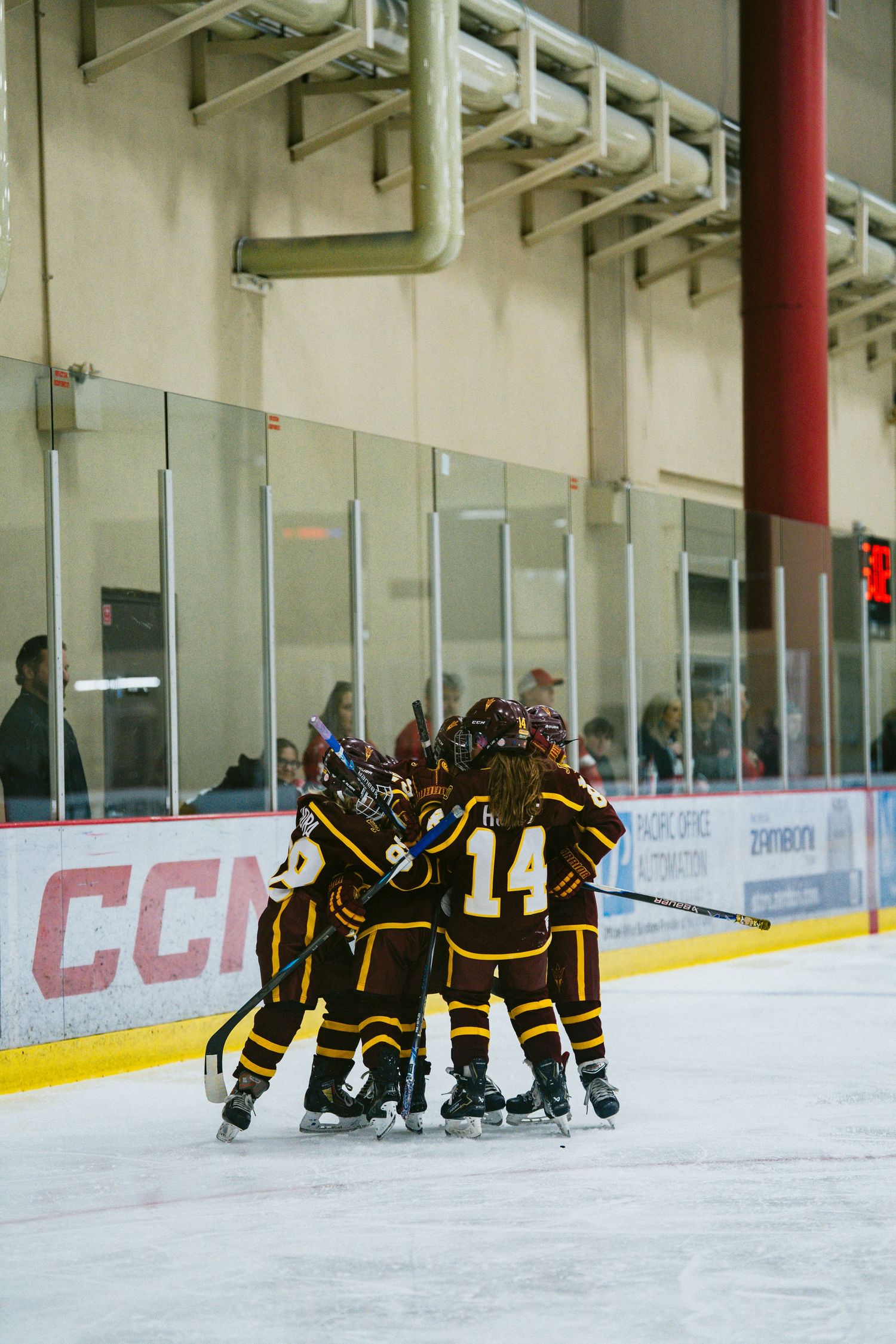 Two hockey teams huddle separately on opposite ends of an indoor ice rink.