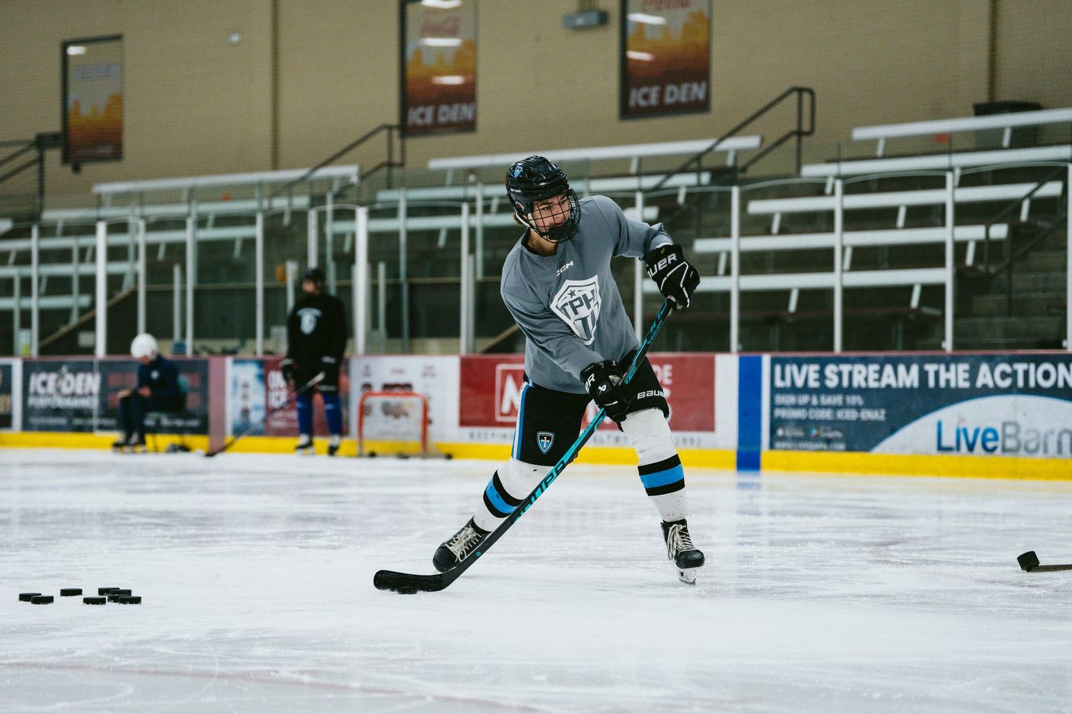 Hockey player in teal jersey skating with puck during practice at Ice Den arena.