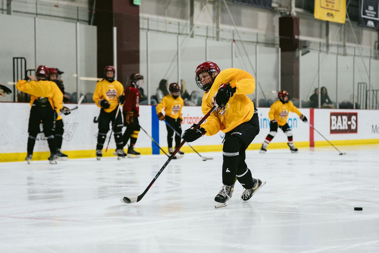 Hockey player in yellow jersey takes a shot on ice during an indoor practice drill.