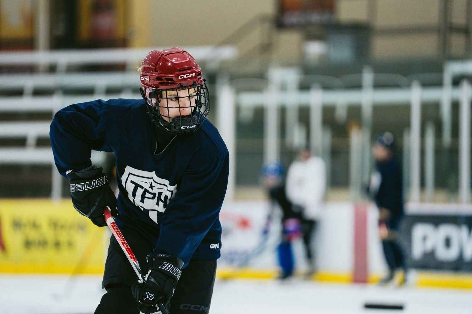 Young hockey player in blue jersey and red helmet handling puck during ice hockey practice.
