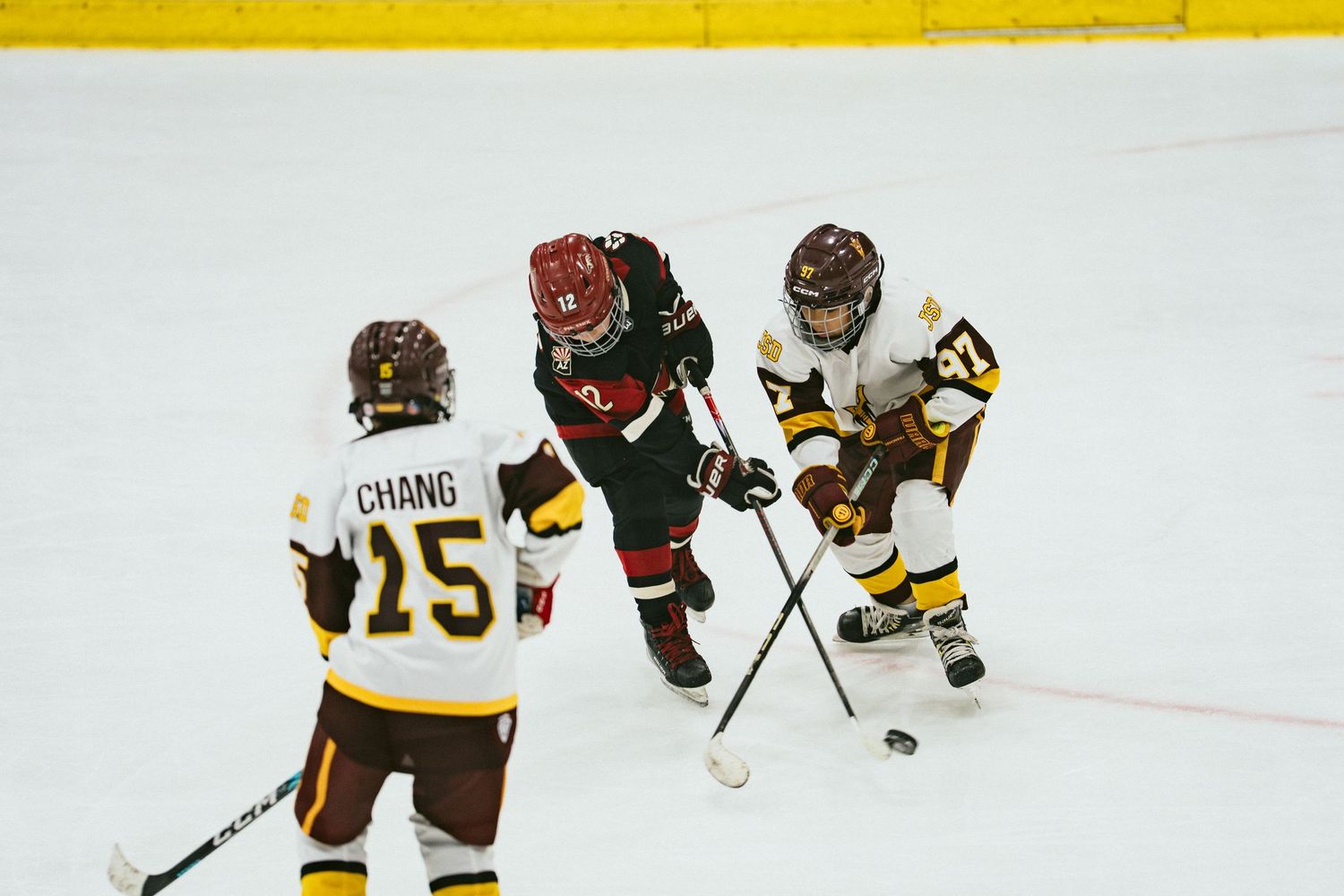 Three ice hockey players battle for the puck during a competitive game, including player CHANG number 15.