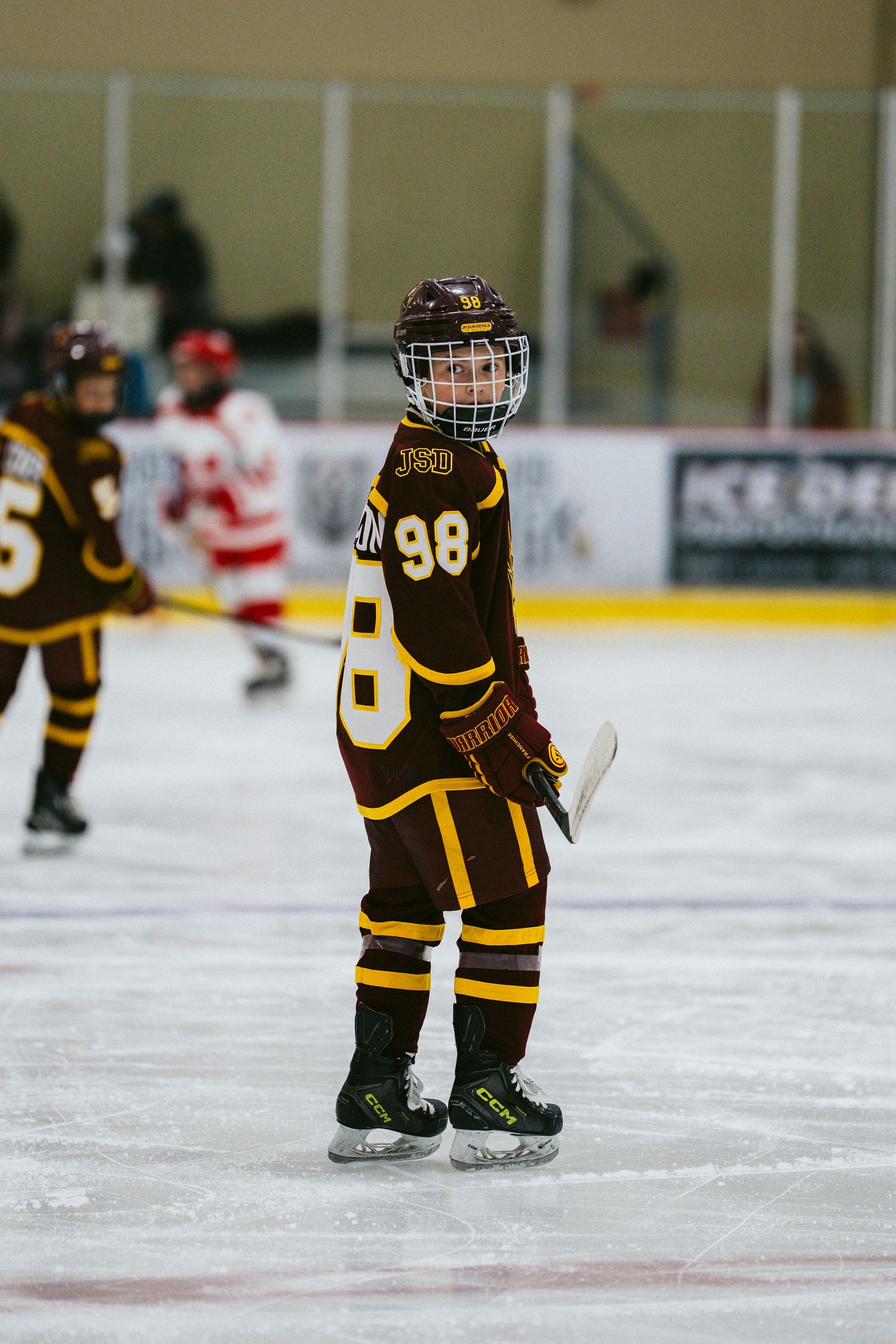 Small hockey players in brown uniforms skate on ice during a youth league game.