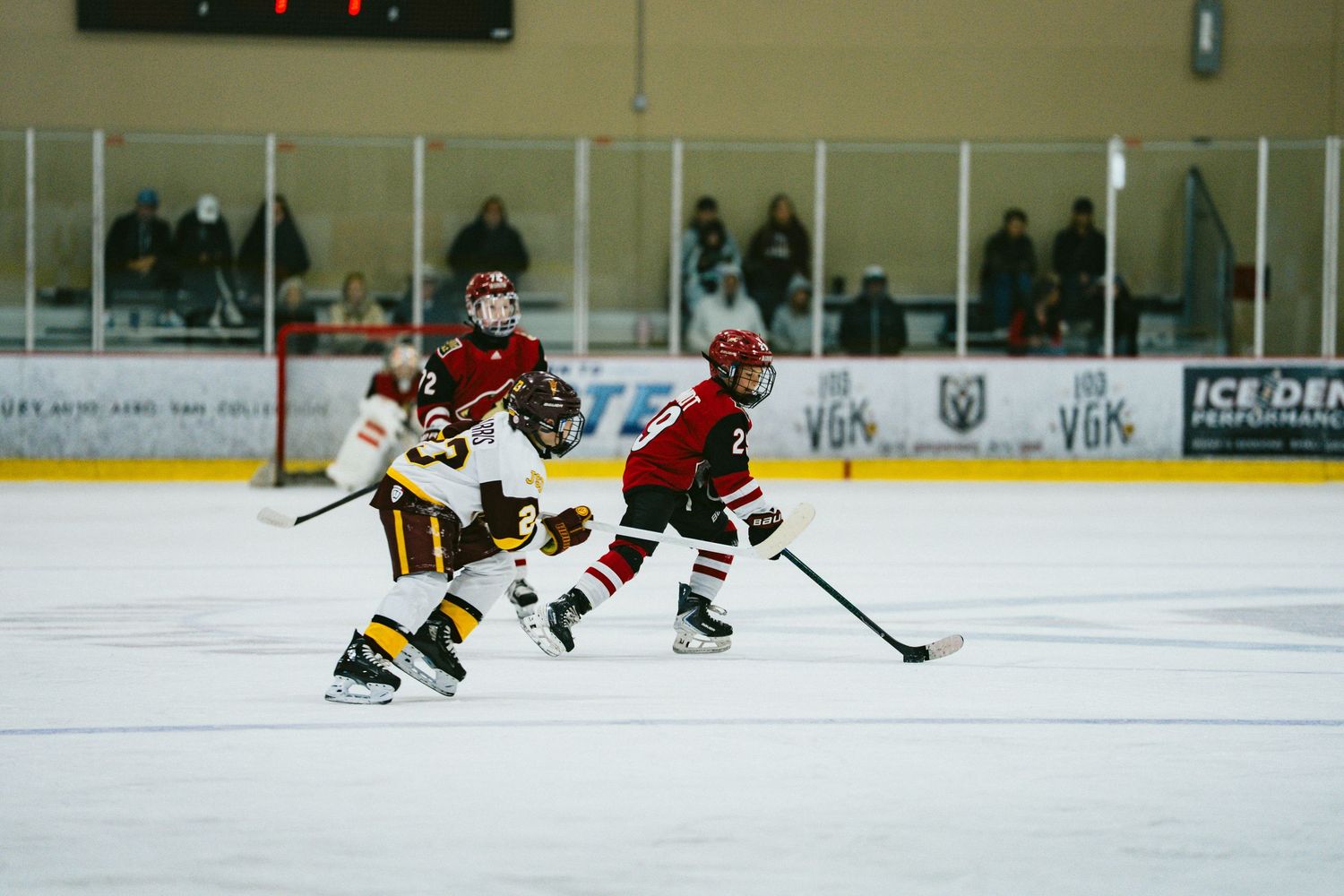 Ice hockey players in red and dark uniforms chase the puck during competitive gameplay.