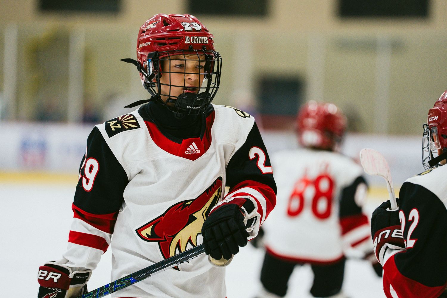 Youth hockey players in red and black jerseys skate during a competitive match on the ice.
