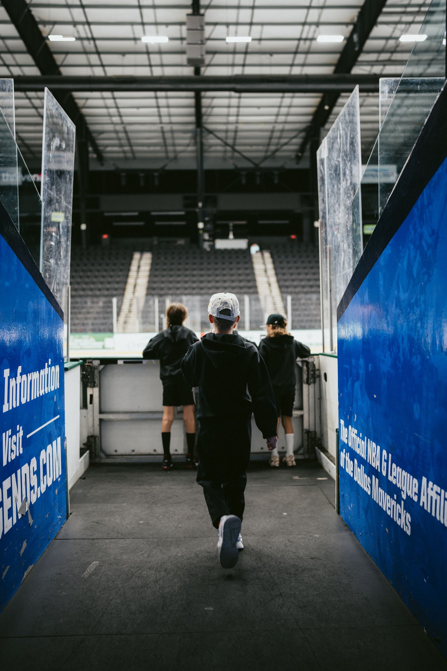 People walking through a dimly lit arena tunnel with blue walls.