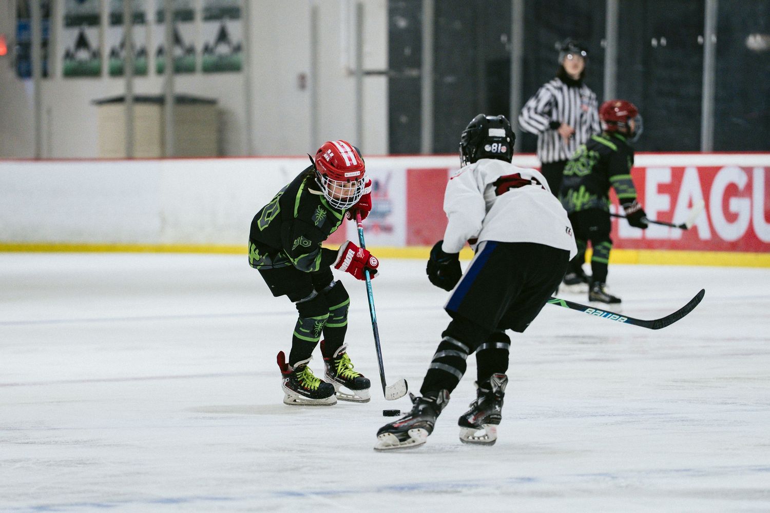 Young hockey players compete for puck during youth ice hockey game with referee watching.
