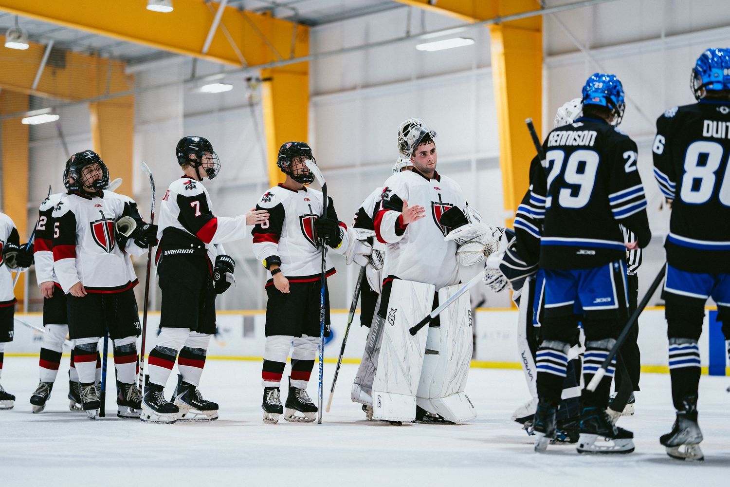 Two hockey teams shake hands on the ice after a game in a yellow-accented indoor rink.