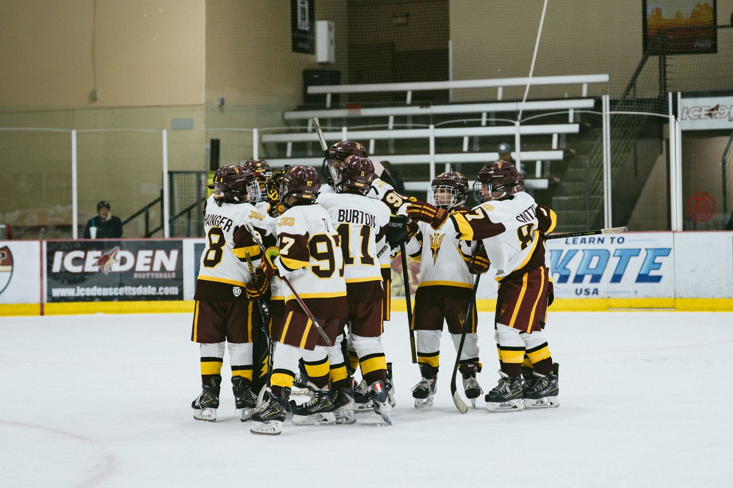 JSD youth ice hockey team huddles together on indoor rink ice during team meeting or celebration.