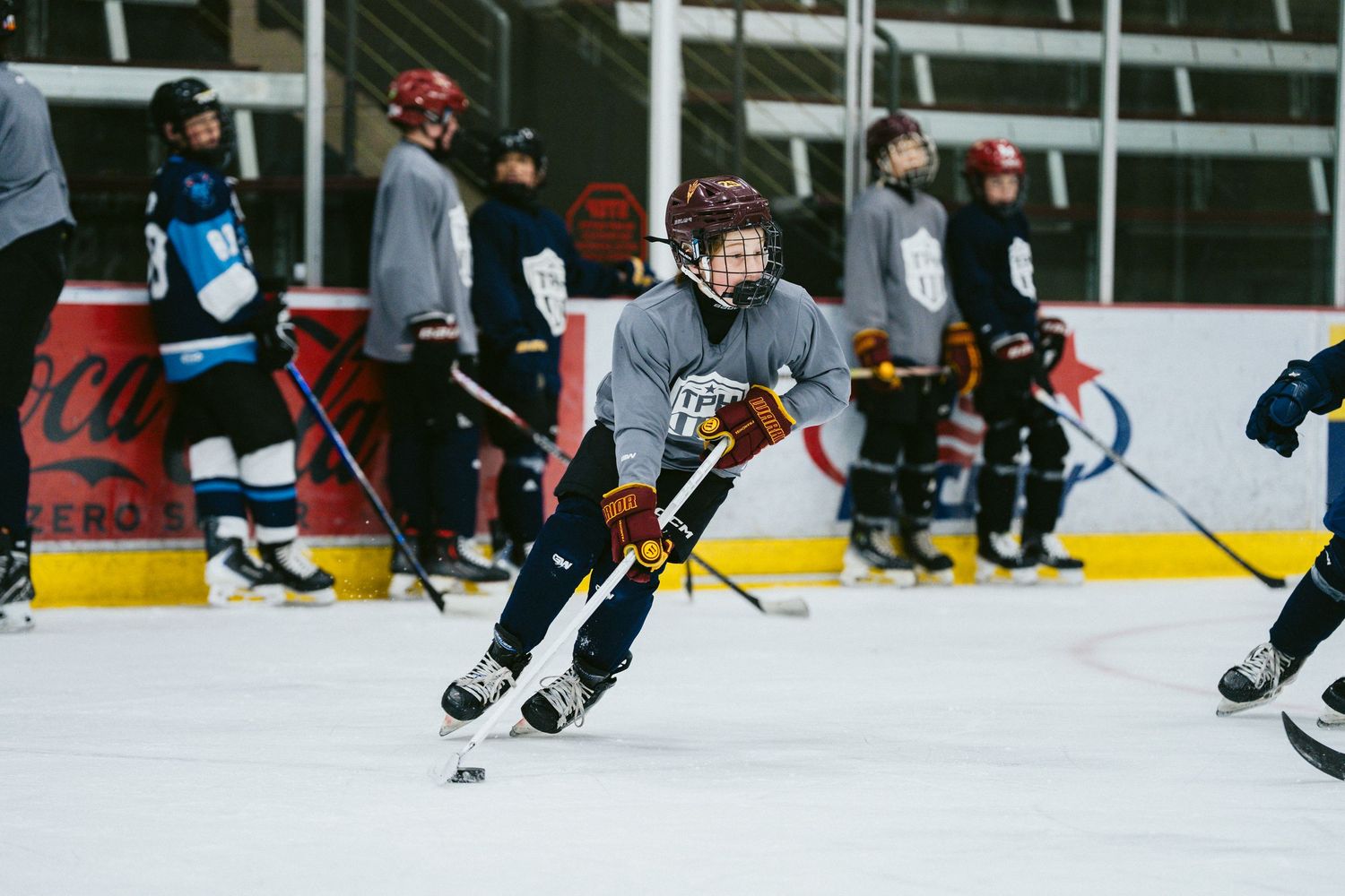 Youth hockey player in red helmet handles the puck during a TPH ice hockey practice session.