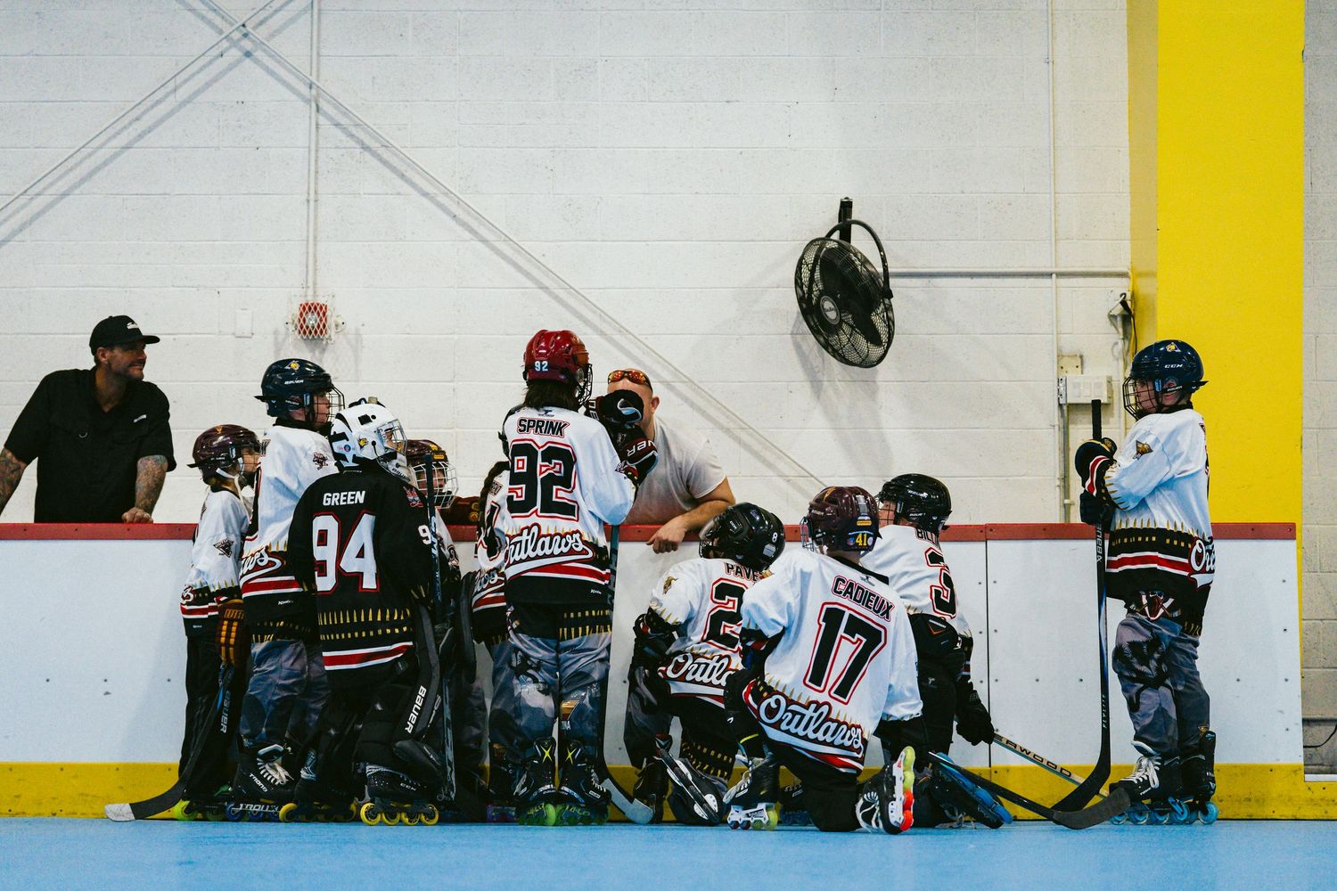 Youth roller hockey team huddles with coaches along the boards during an indoor game timeout.
