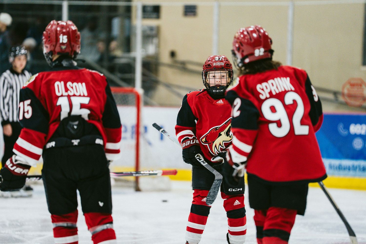 Youth hockey players in red jerseys skate on ice during a game.
