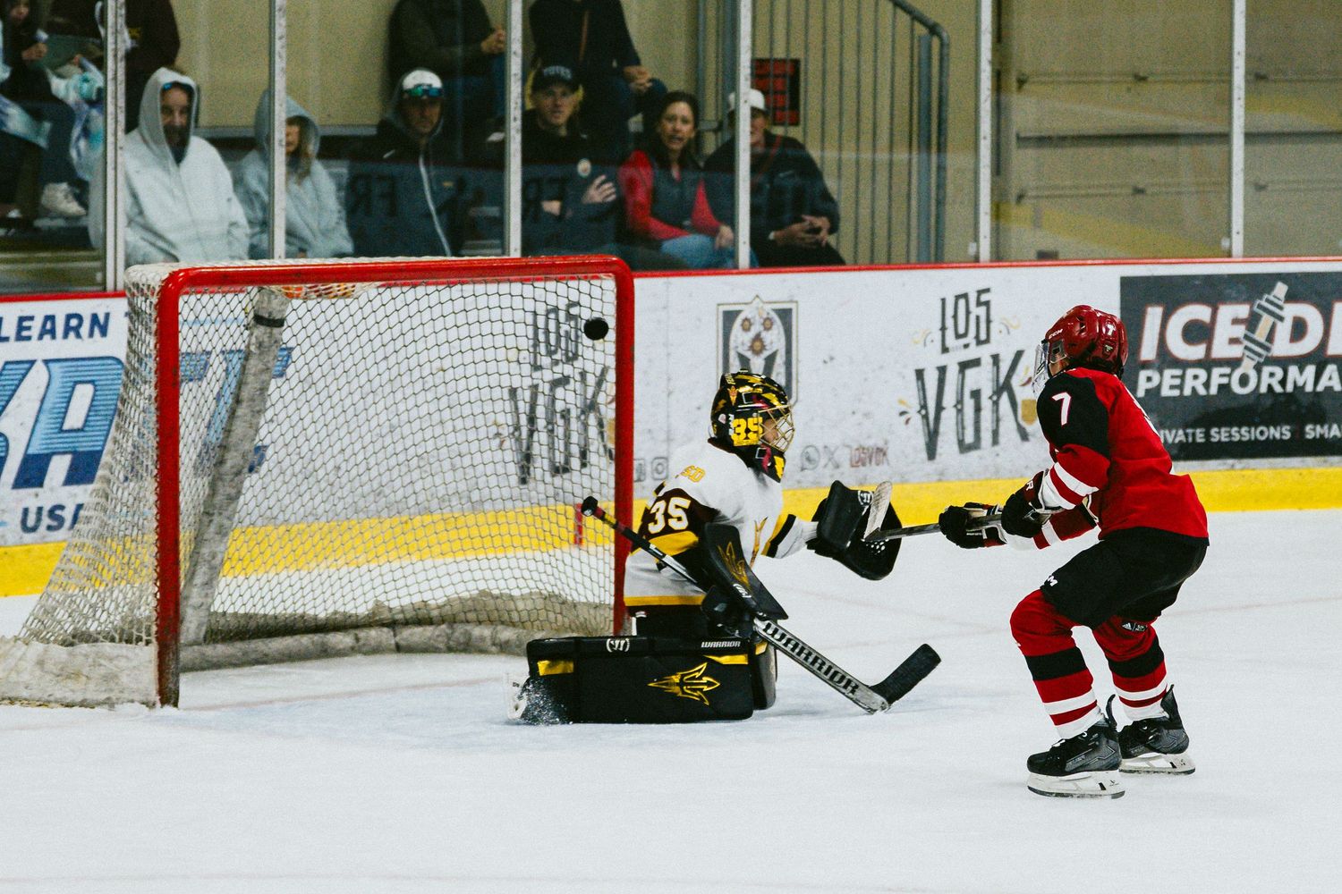 Ice hockey players compete for the puck near the goal net during an intense game moment.