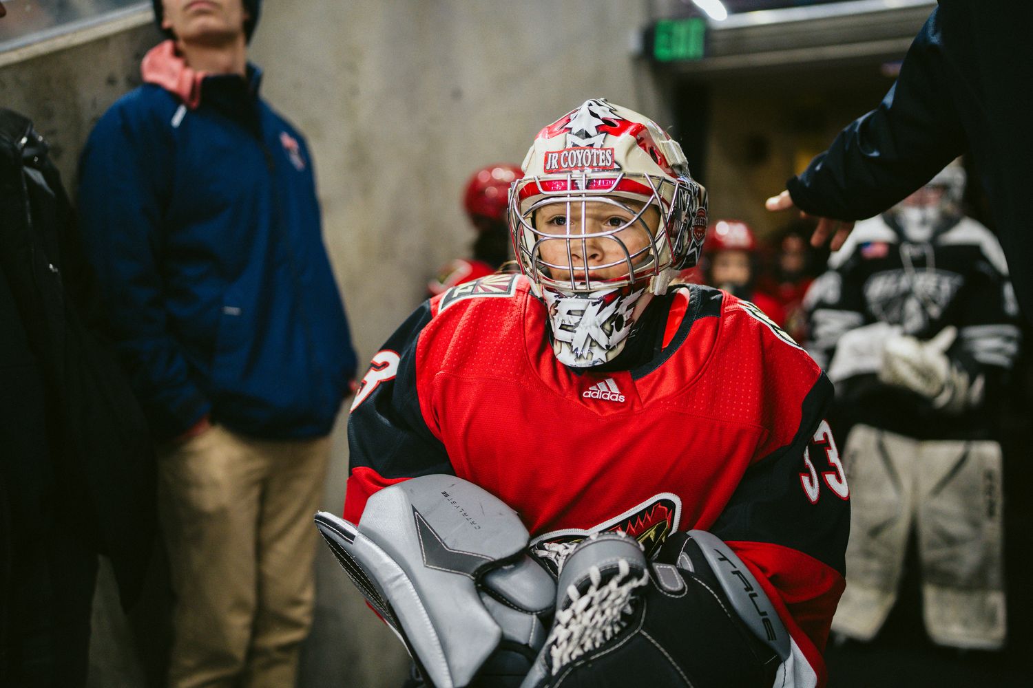 Hockey goalie in red jersey and protective mask in arena hallway.