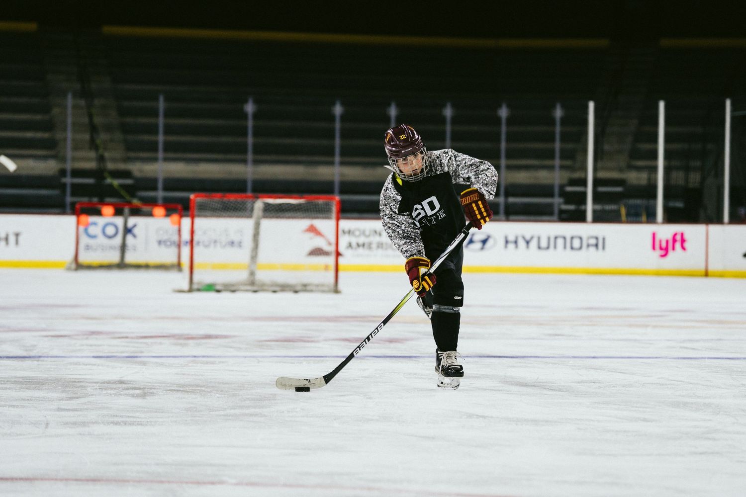 Youth hockey player in camo jersey handles the puck alone on a professional indoor ice rink.