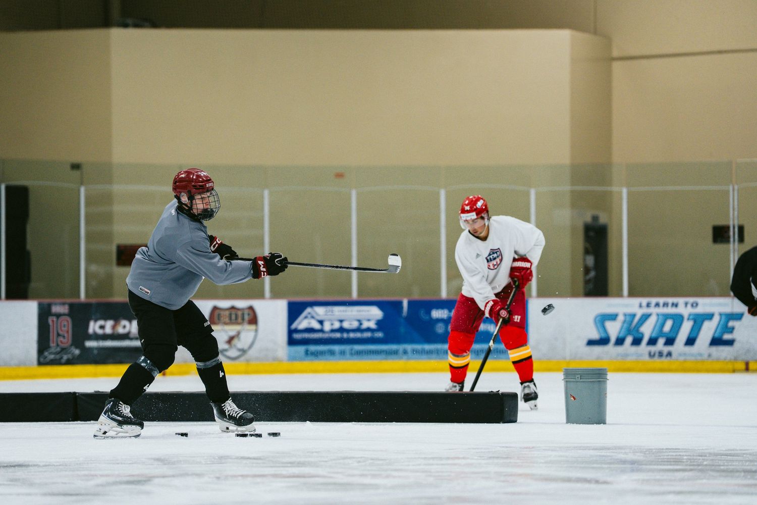 Two hockey players practicing passing and shooting drills on indoor ice rink.