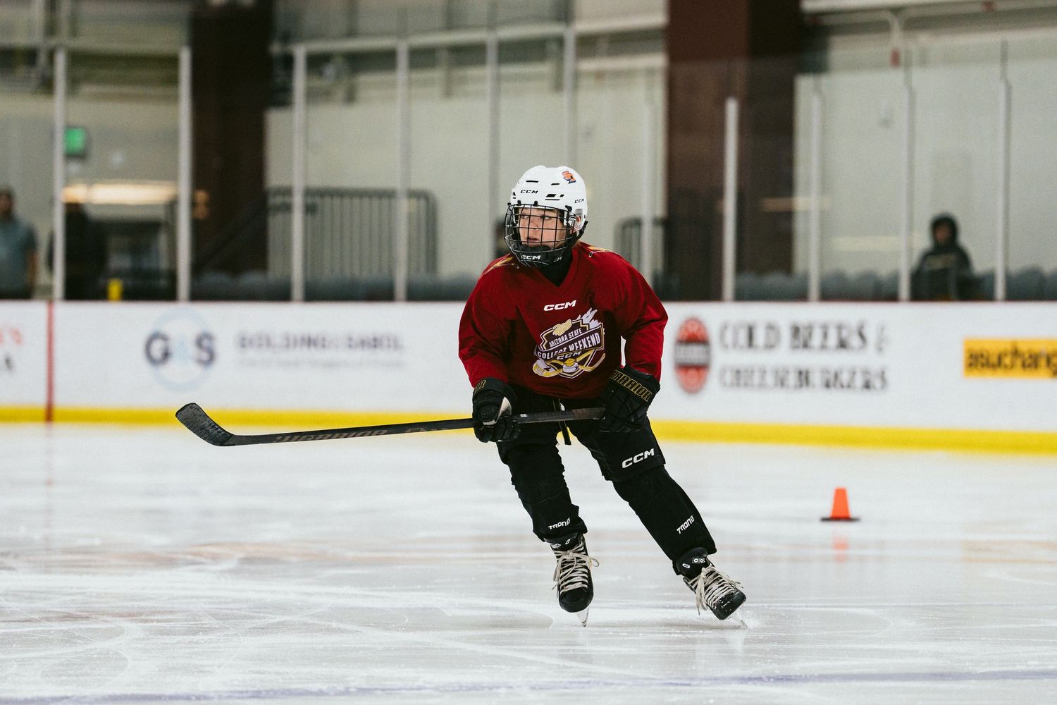 Young hockey player in red jersey skates around an orange cone during a youth ice hockey skills drill.