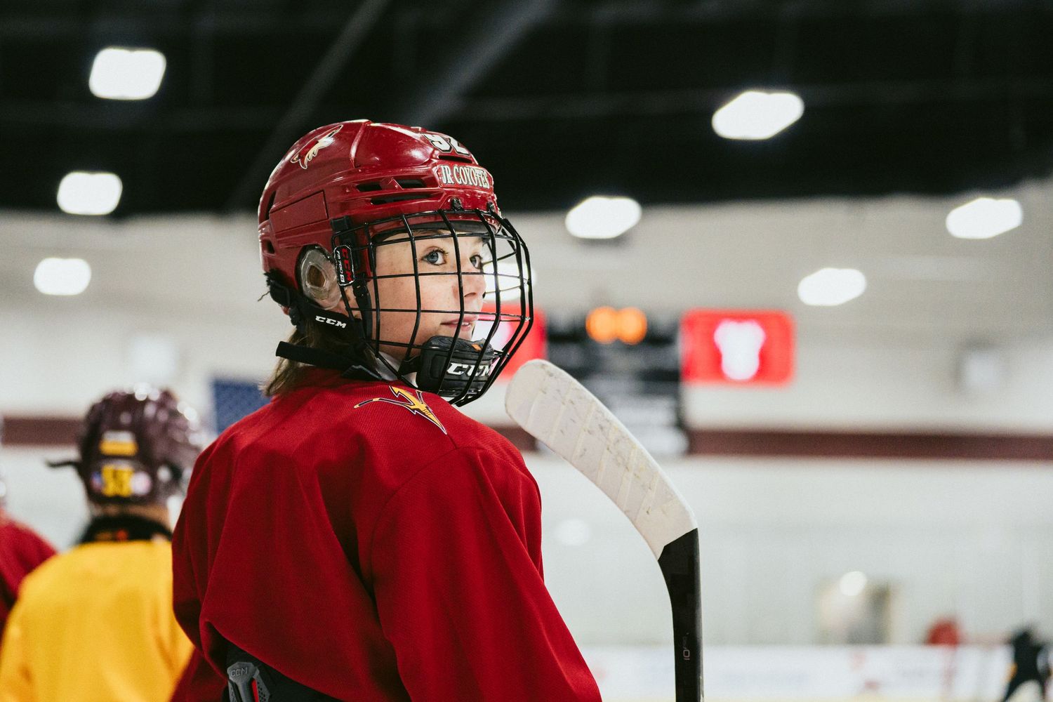 Young hockey player in red helmet and jersey looks over shoulder on ice rink during practice.