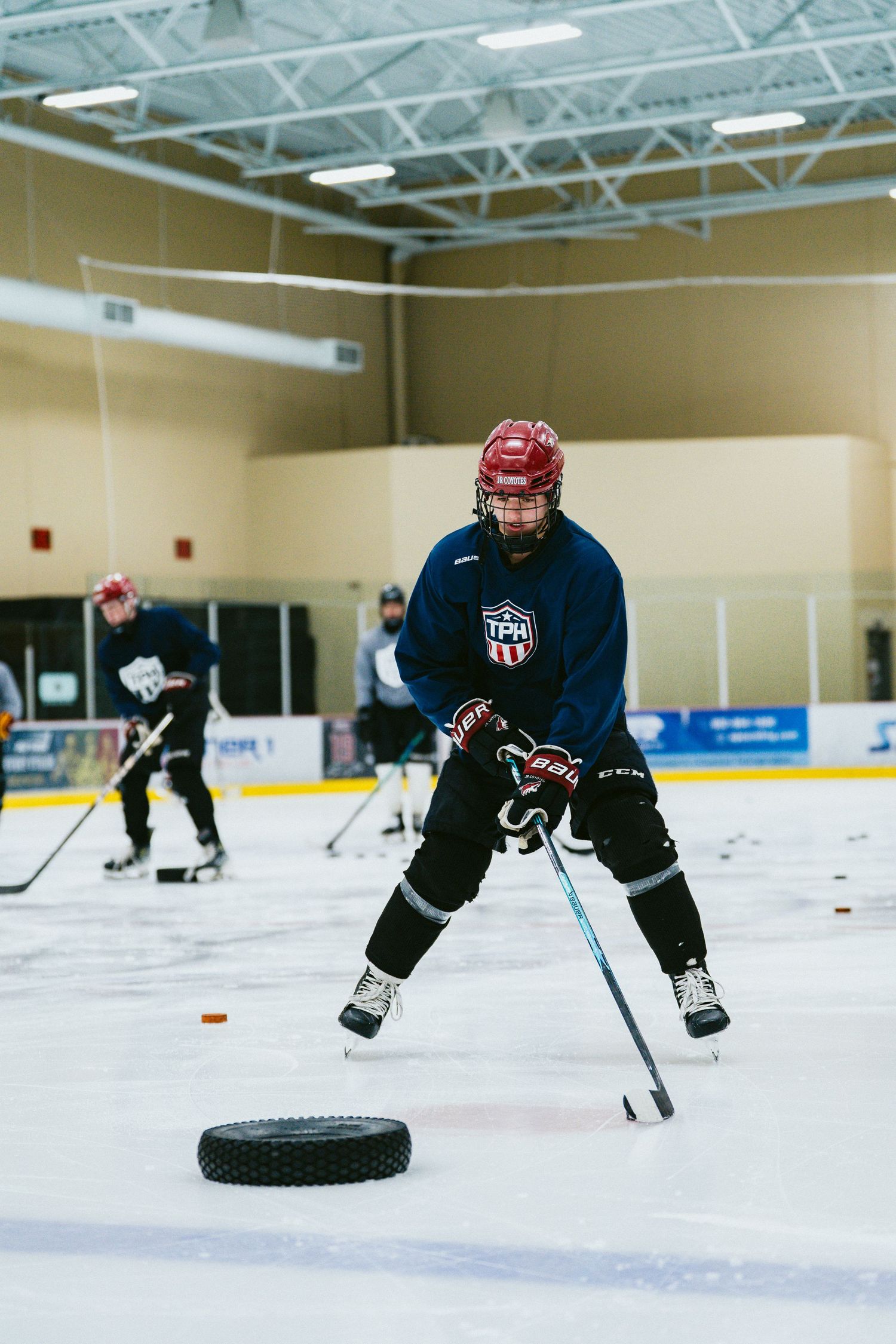 Youth hockey player in red helmet practices puck handling drills on indoor ice rink during training.