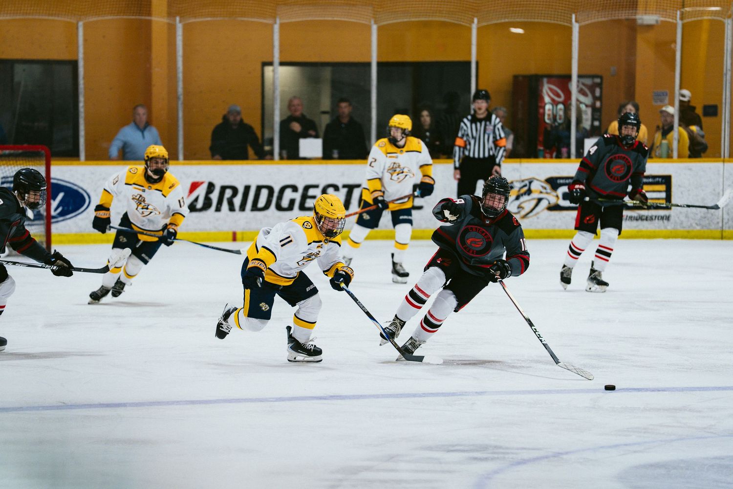 Youth hockey players compete on ice as a referee watches during an indoor hockey game.