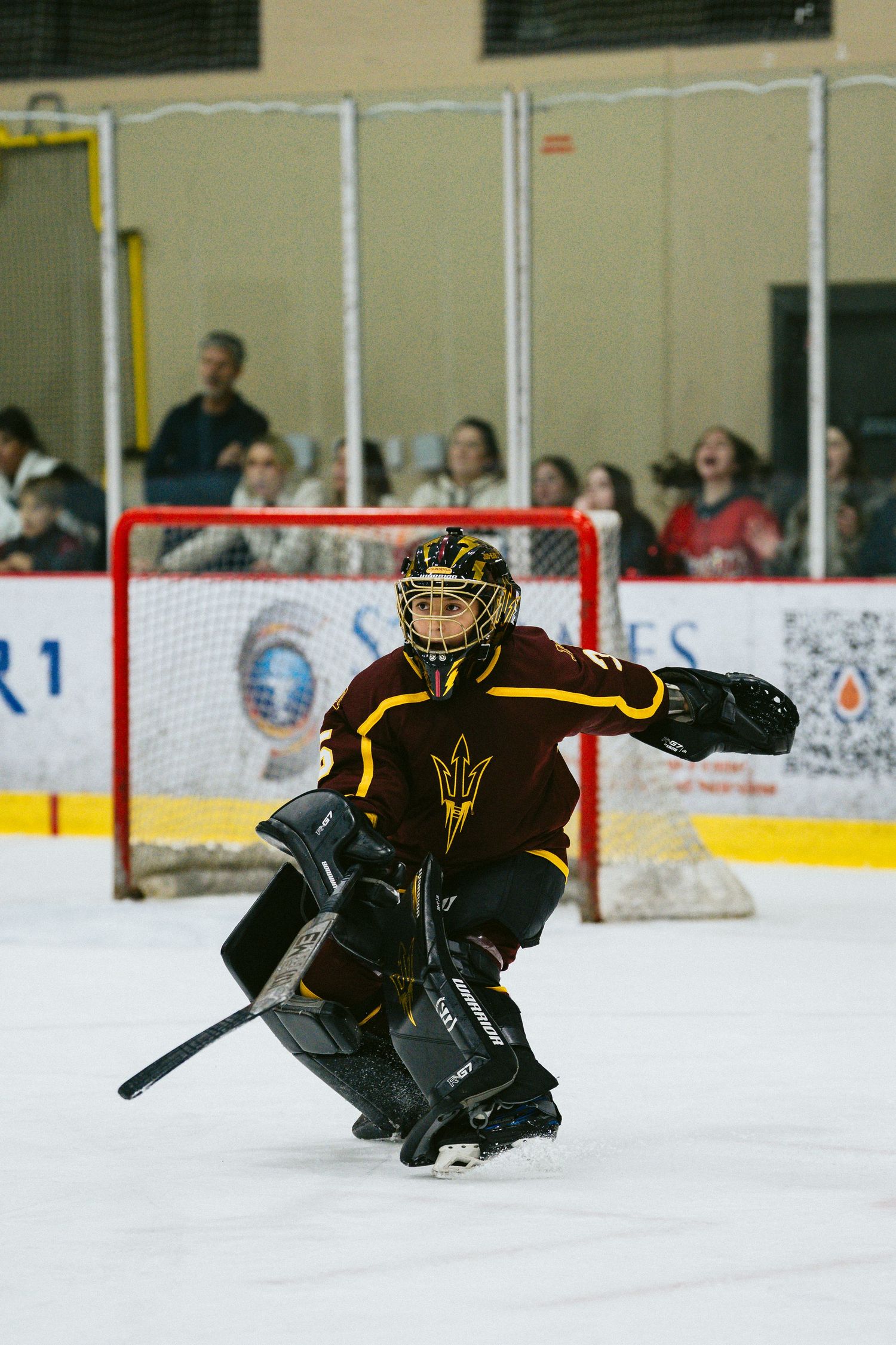 Goalie in protective gear makes a dramatic save on the ice during a hockey game.