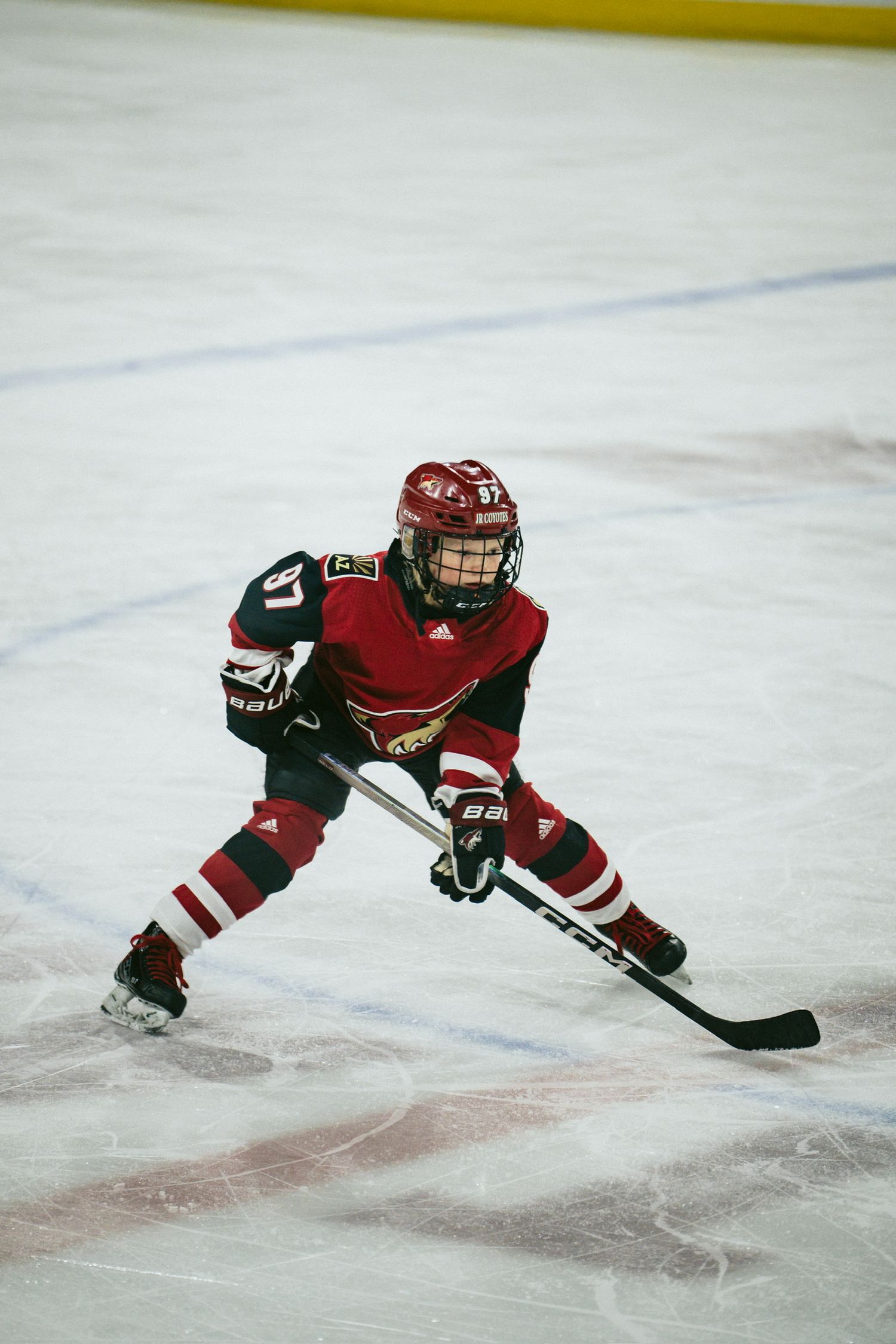 Young hockey player in red jersey skates low to the ice during practice.