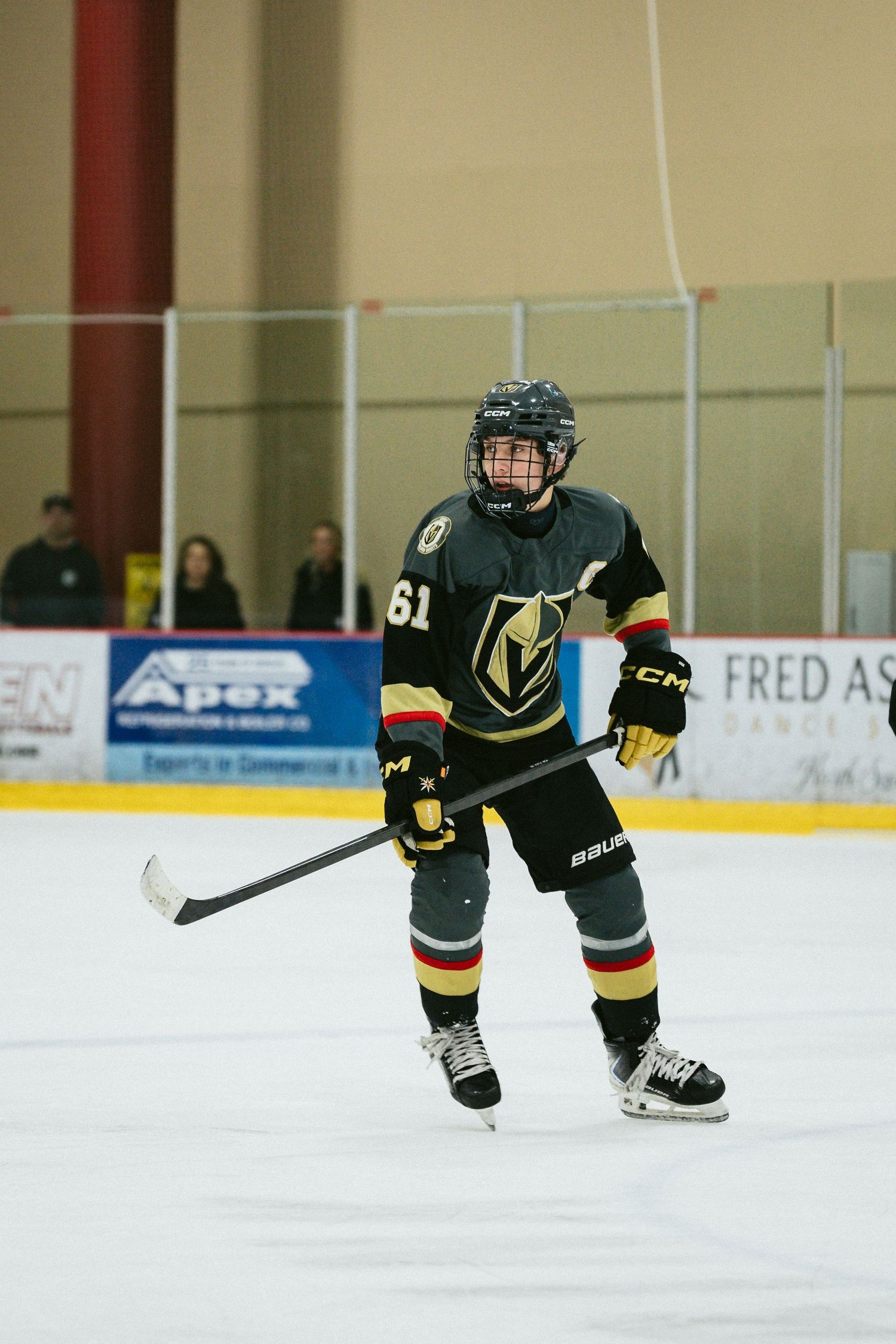 Players in black and gold uniforms skate across the ice during a hockey game.