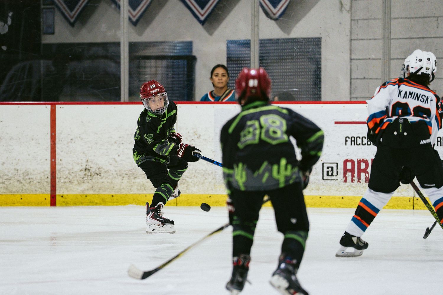 Young hockey players compete on ice, with one player passing the puck during a youth hockey game indoors.