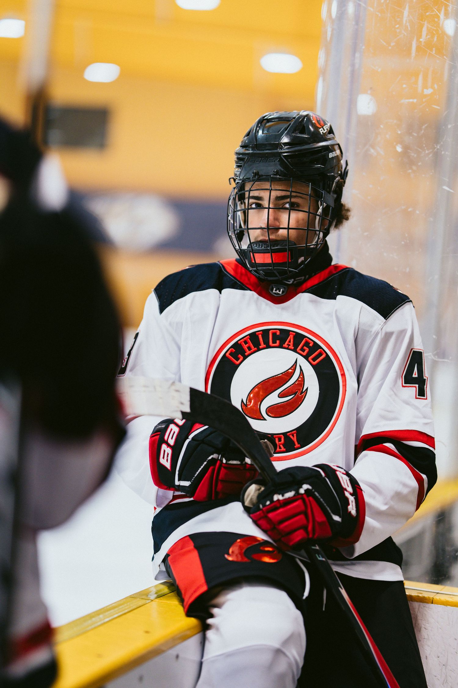 Young hockey player in Chicago Fire white jersey sits against the boards during an indoor ice hockey game.
