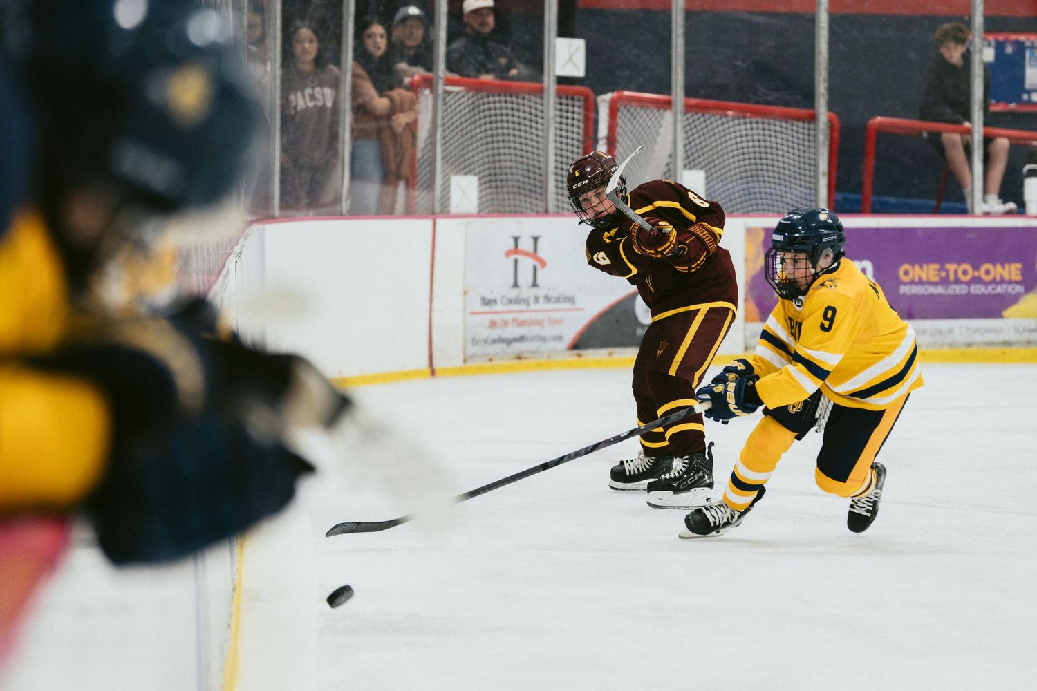 Hockey player in yellow jersey number 9 battles for puck against maroon-uniformed opponent during indoor ice hockey game.