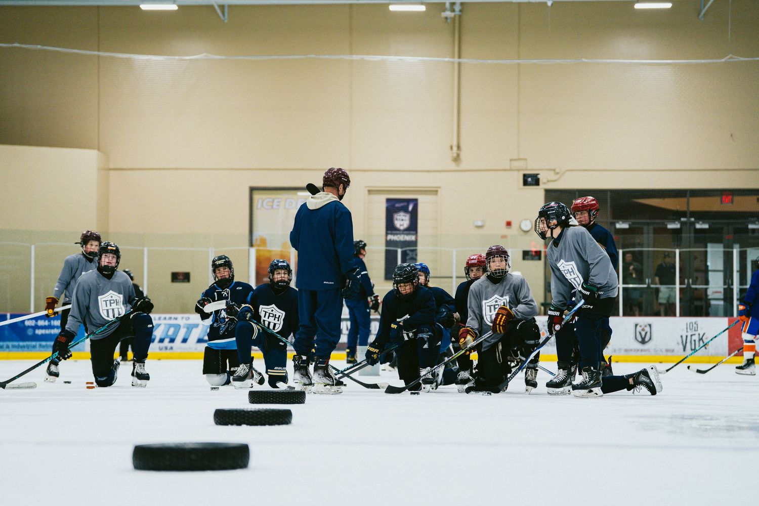 Youth hockey players practice drills on ice rink during team training session with coach.