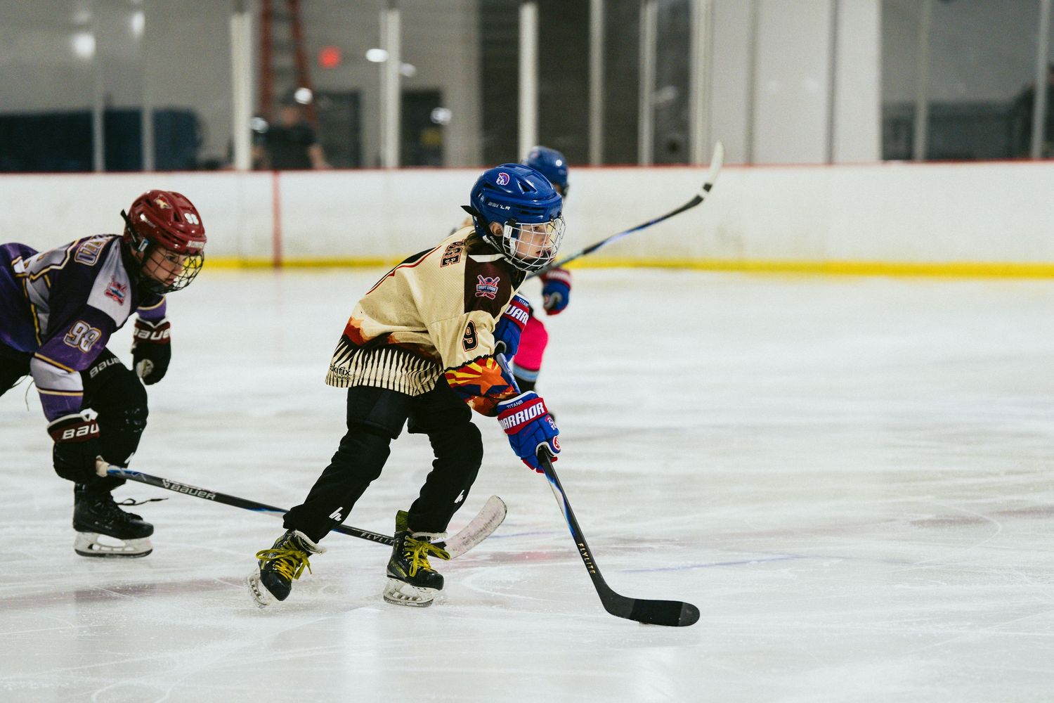 Three young hockey players compete for puck possession during a youth ice hockey game.