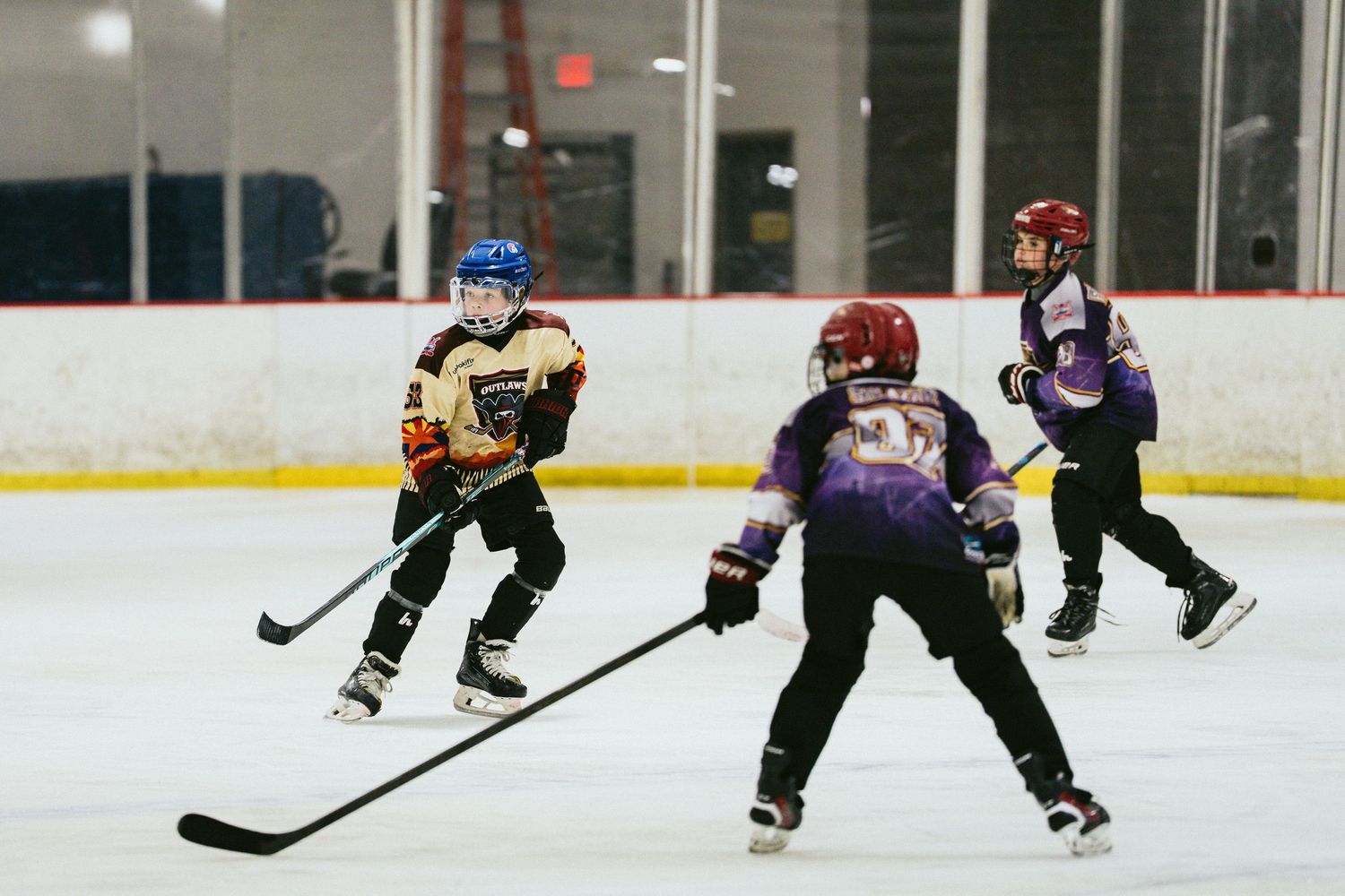 Three young hockey players skate during a youth ice hockey game on an indoor rink.