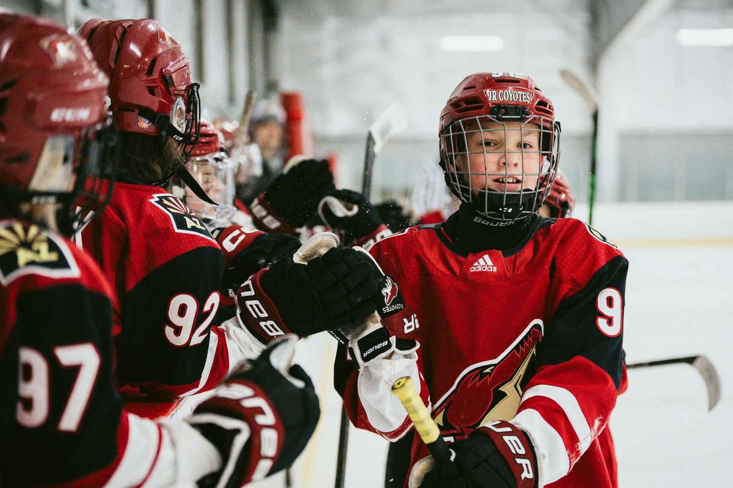 Young youth hockey players in red jerseys fist-bumping teammates on the ice during a game.