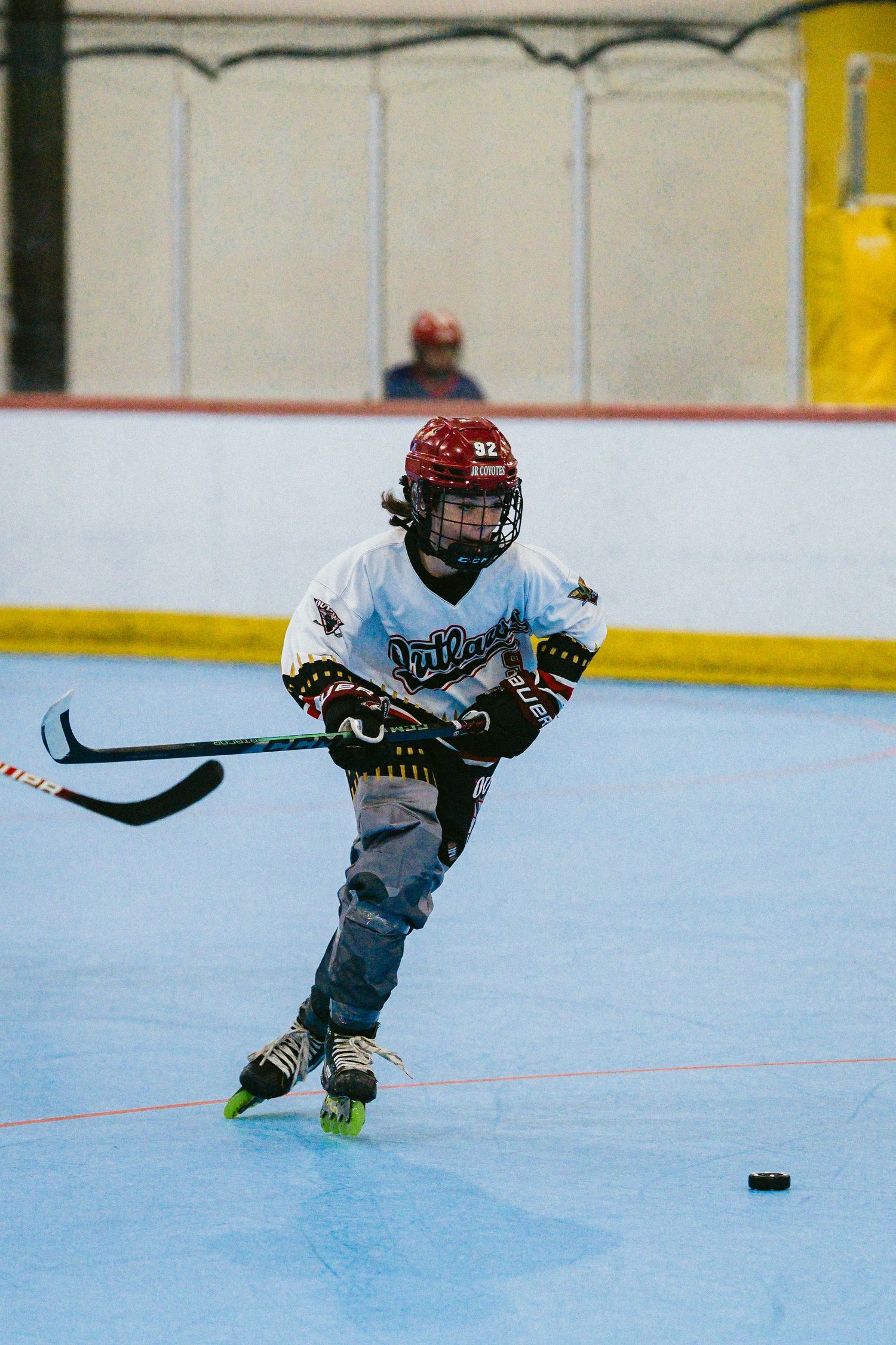 Young roller hockey player in white Outlaws jersey controls the puck during an indoor inline hockey game.