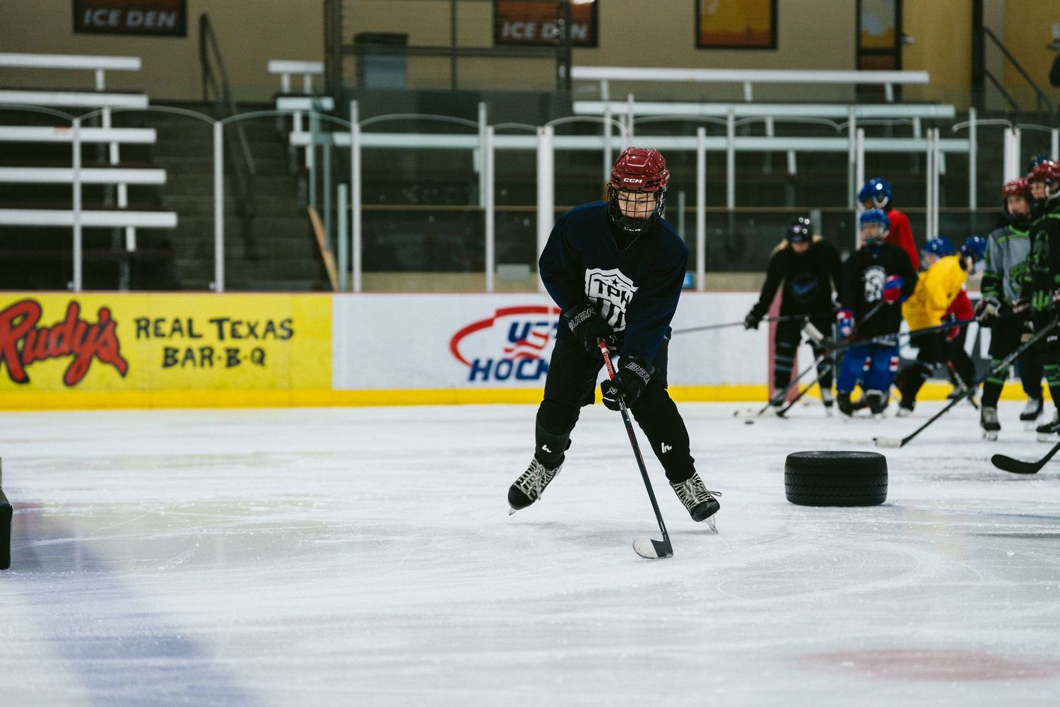 Young hockey player in black jersey handles puck on indoor ice rink during practice drill.