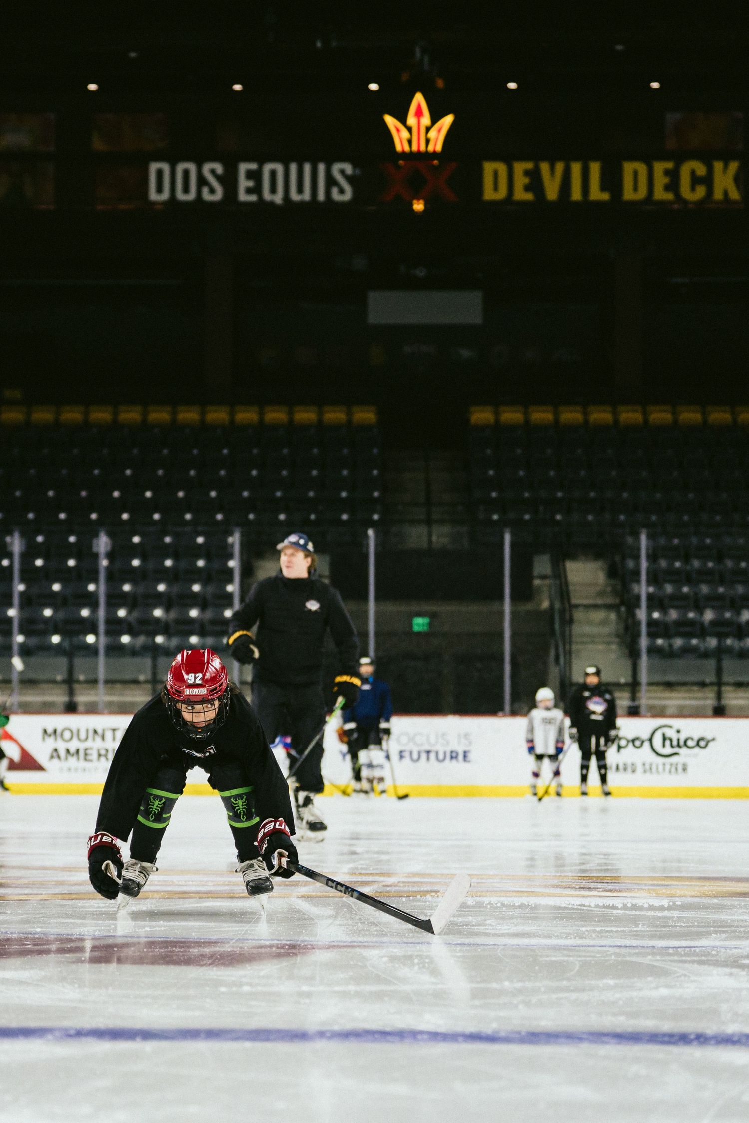 Hockey player crouches low on ice during practice at Arizona State University arena with Dos Equis Devil Deck signage.