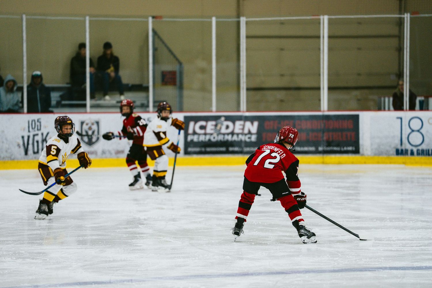 Youth hockey players compete in an ice rink during a game with players wearing red and yellow jerseys.
