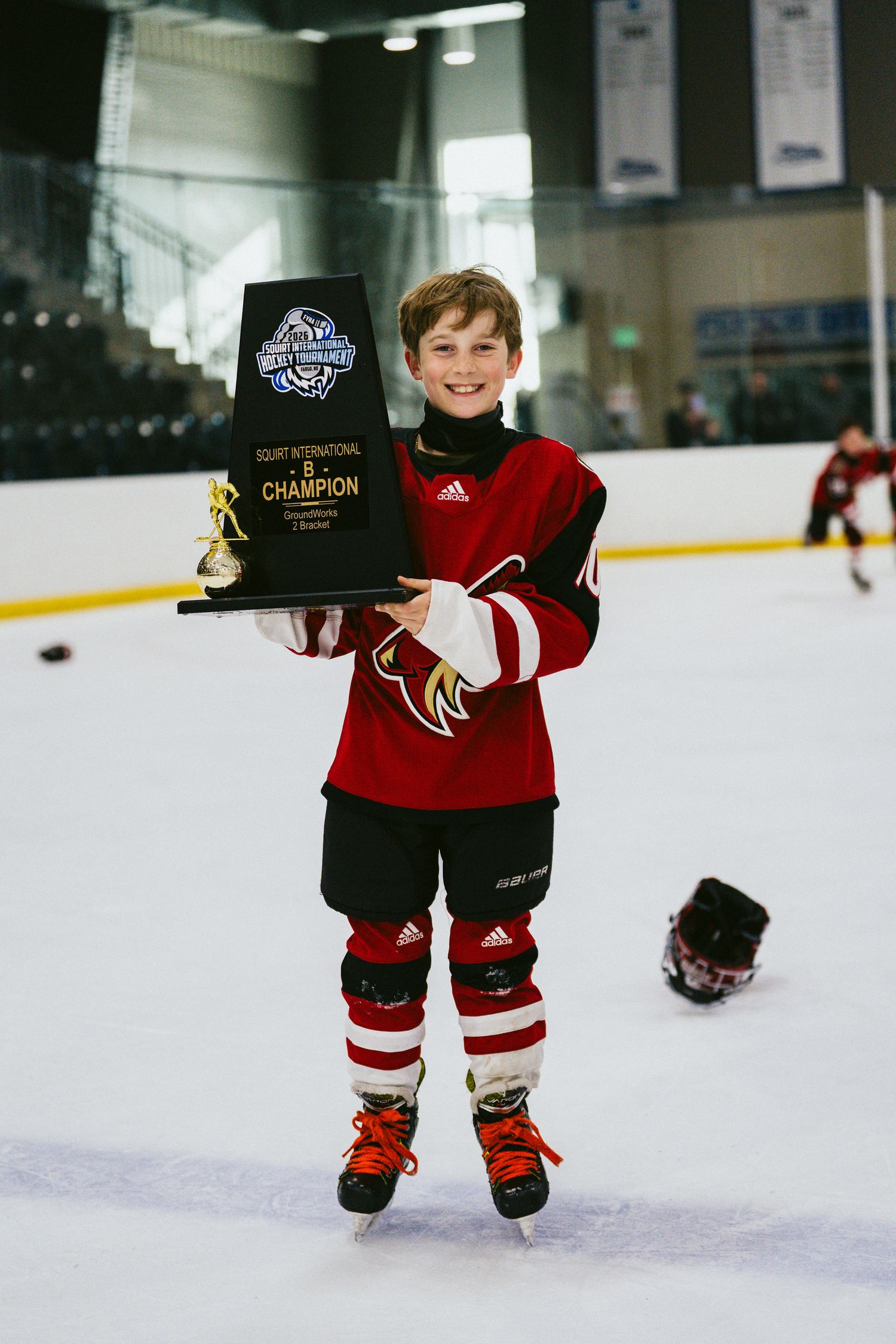 Young hockey player in red jersey displaying championship award while skating.