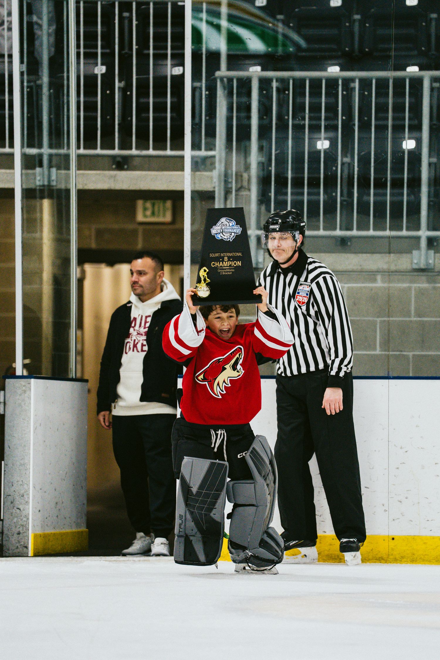 Hockey officials in striped uniforms watching players on ice rink during practice.