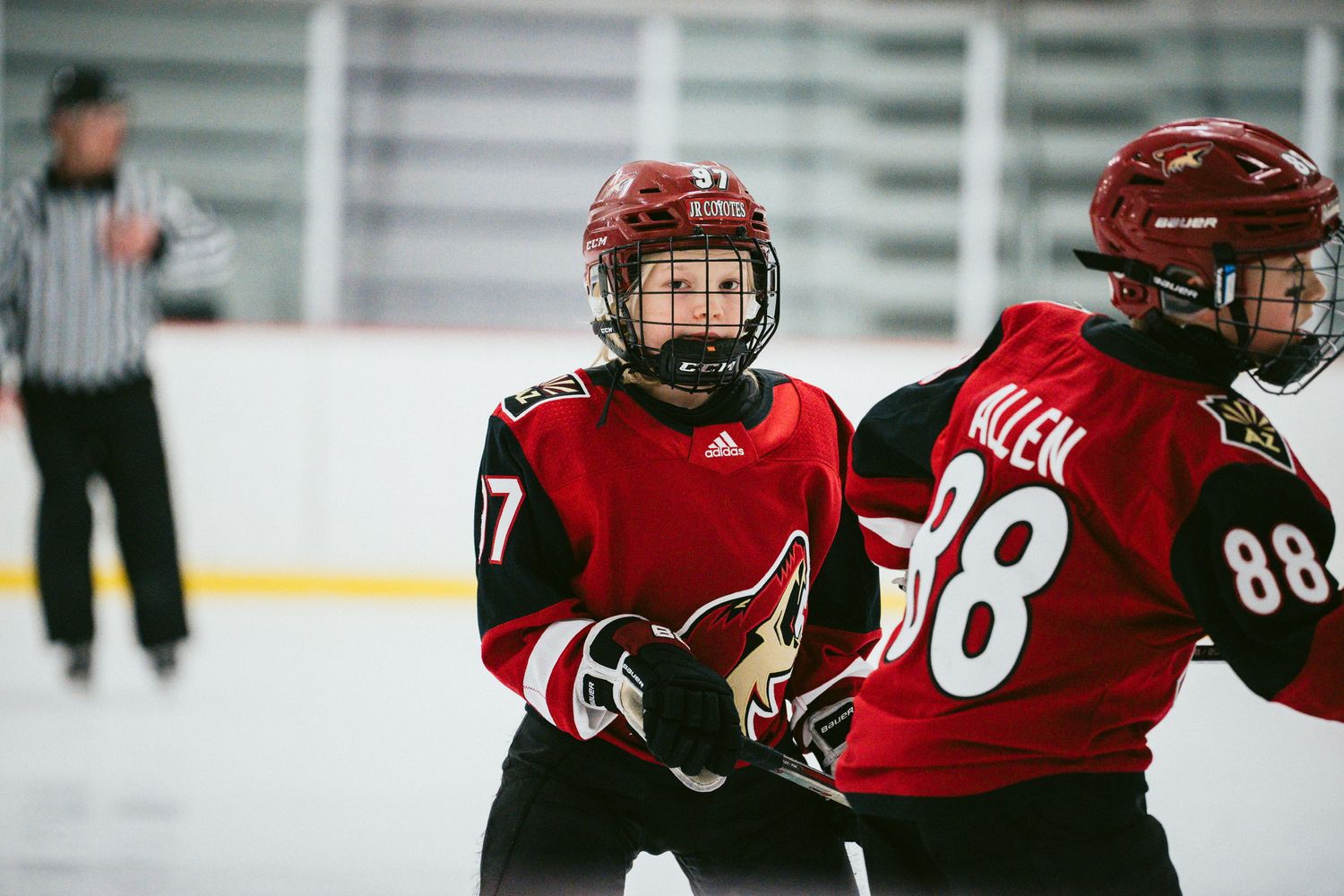Youth hockey players in red jerseys practicing drills on ice rink.