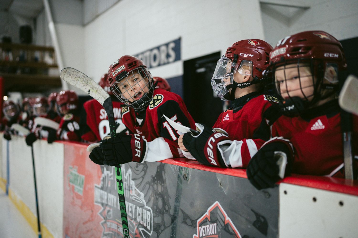Hockey players lean against the boards watching the game from their bench area.