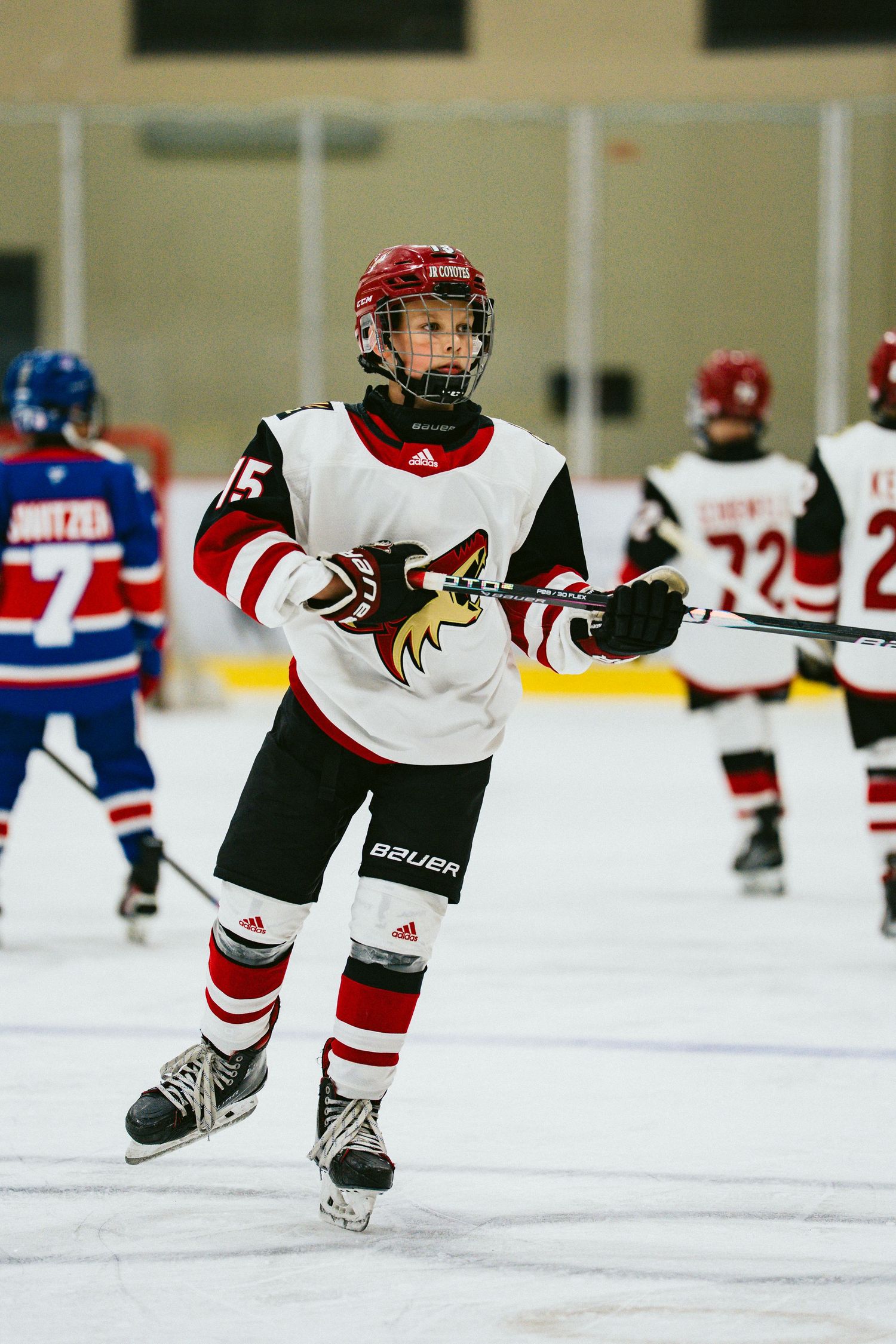 Youth hockey player performs skating drill on ice in red and white uniform.