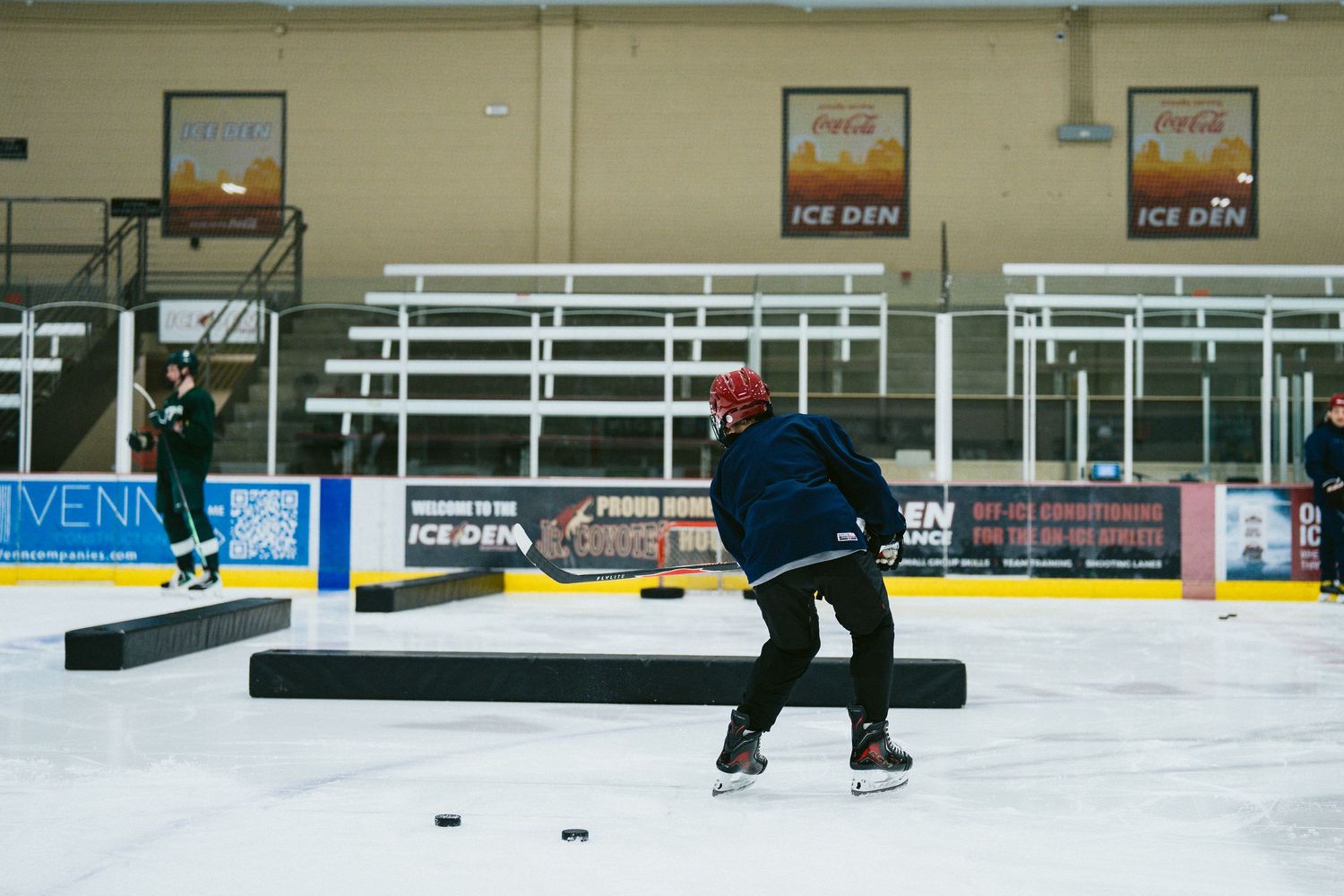 Hockey player skating on ice rink during practice drill at Ice Den arena.
