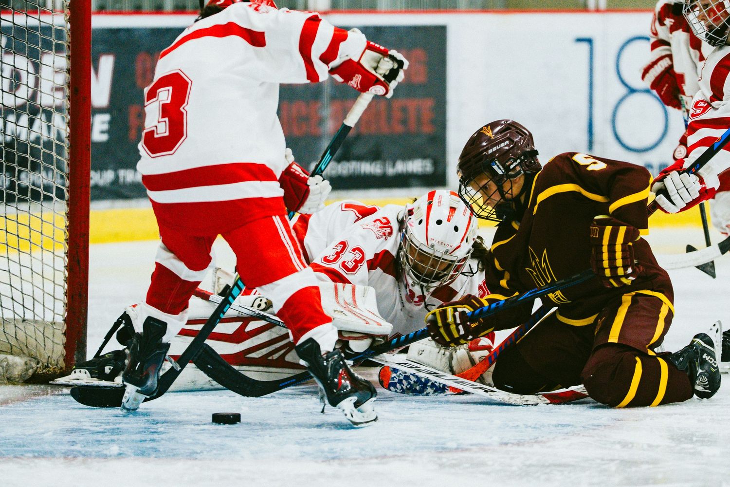Hockey players scramble for the puck during an intense game with red and black uniformed teams on the ice.