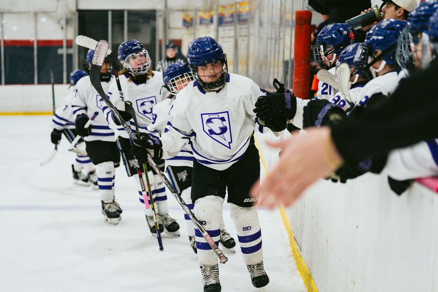 Hockey players in blue jerseys practice skating drills across the ice rink.