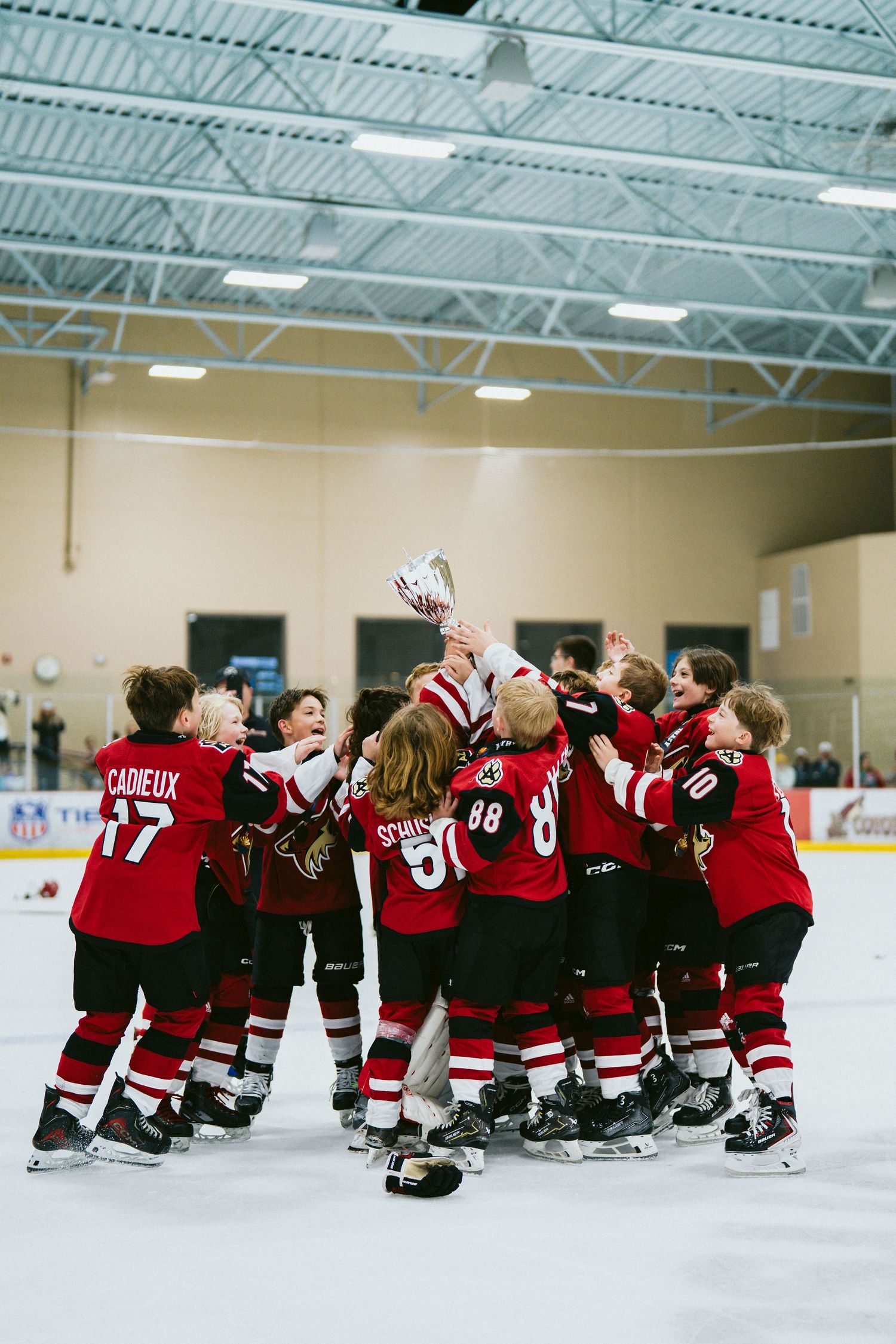 Youth hockey team celebrates on ice by sitting in a line formation wearing red jerseys.