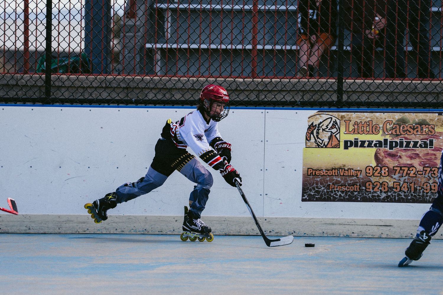 Young roller hockey player skating aggressively toward puck on outdoor rink.
