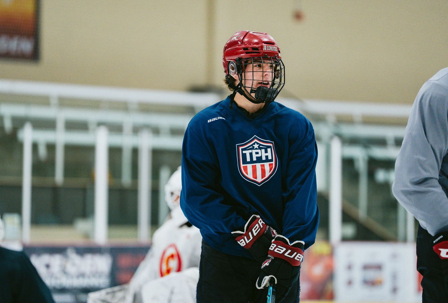 Hockey player in TPH jersey and red helmet stands on ice during practice session.