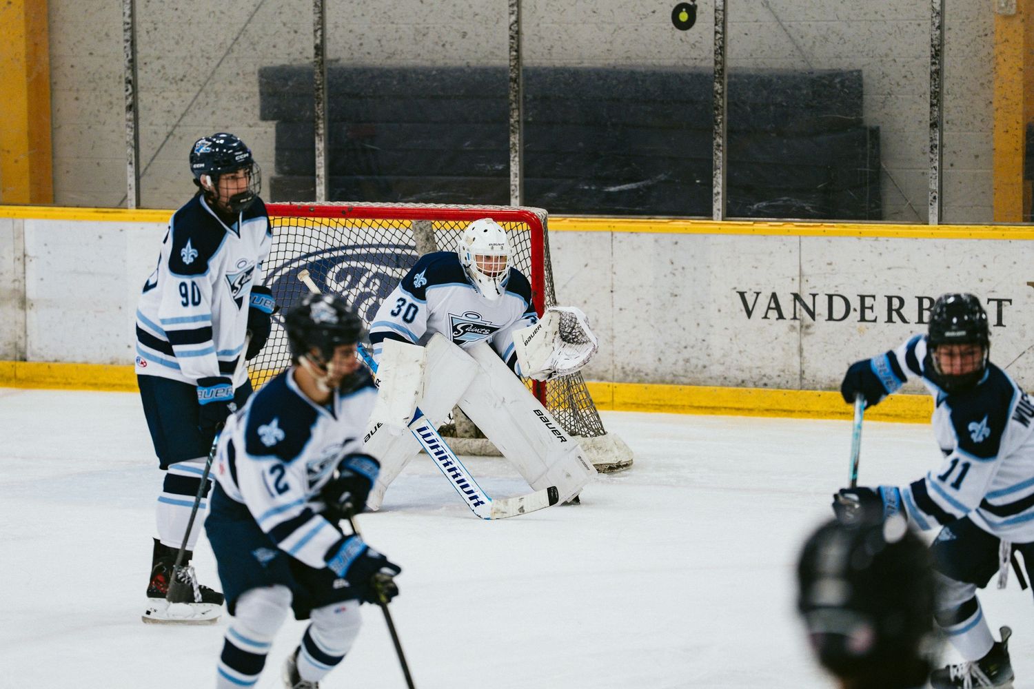 Vanderbilt ice hockey players in white uniforms compete on indoor rink with goalie defending the net.