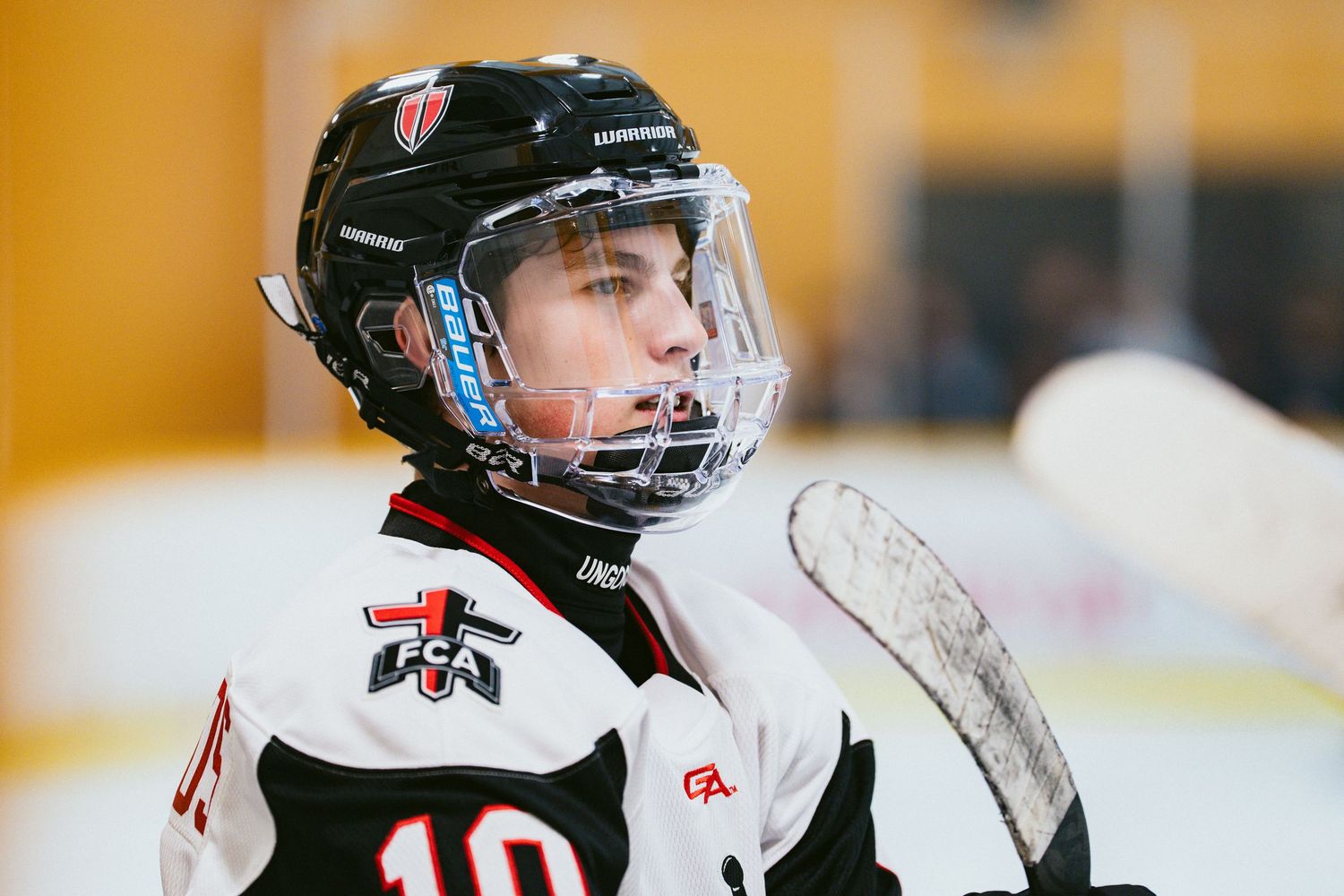 Young ice hockey player in white and black uniform looks up during a game on the rink.